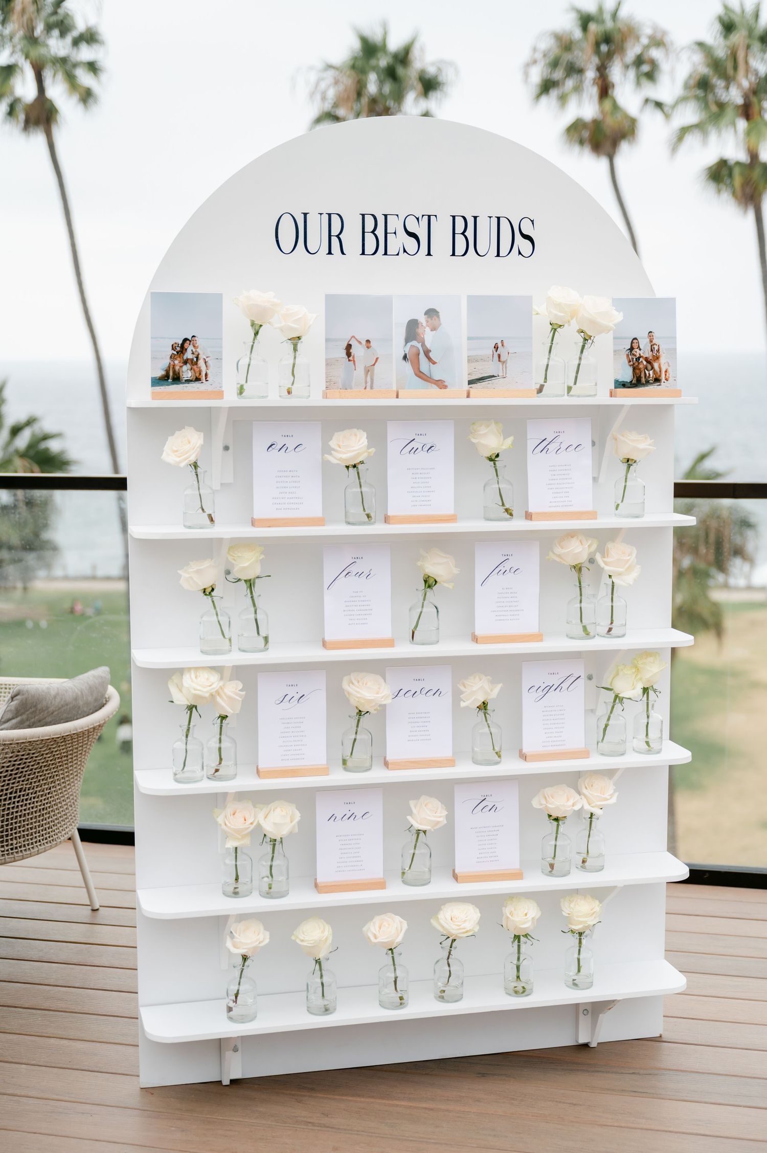 White display shelf with single roses in vases and table assignments labeled 'Our Best Buds'.