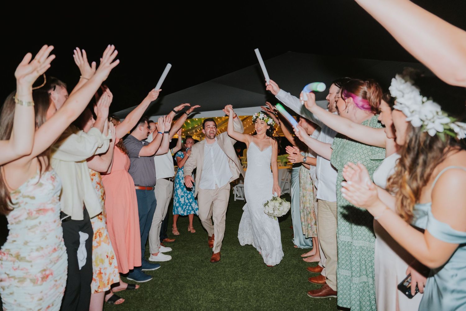Wedding guests forming a celebratory tunnel with raised arms at an outdoor evening reception.
