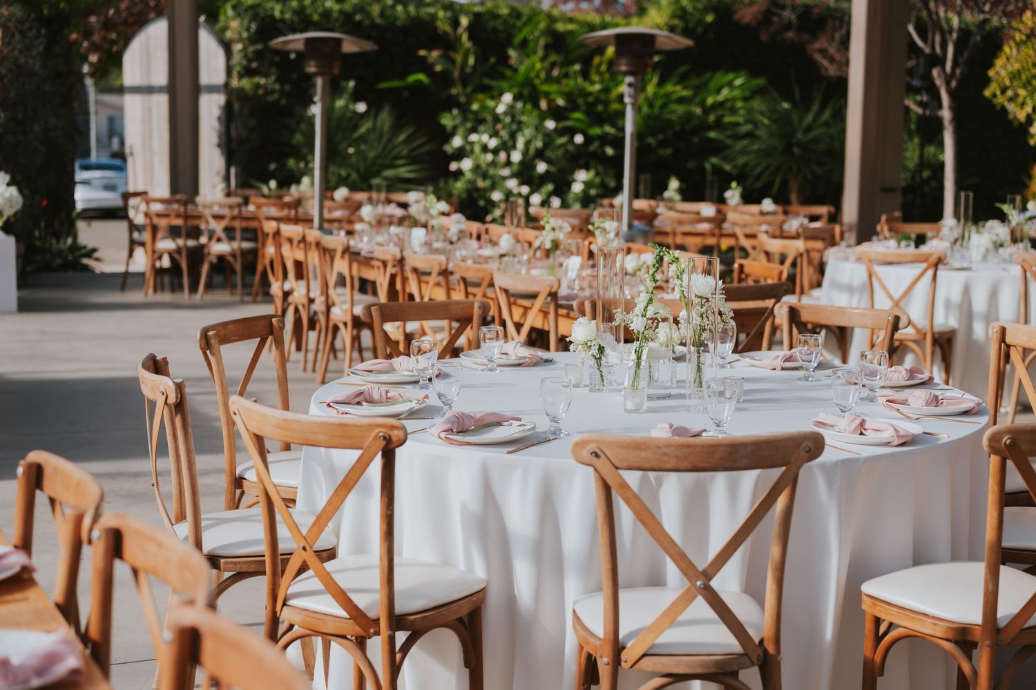 Elegant outdoor wedding reception setup with rustic wooden chairs and white tablecloths under string lights.