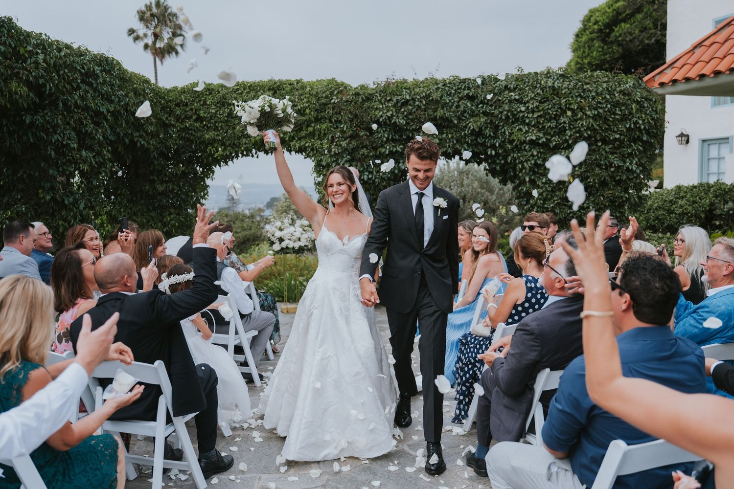 Wedding guests release white balloons into the sky during an outdoor garden celebration.