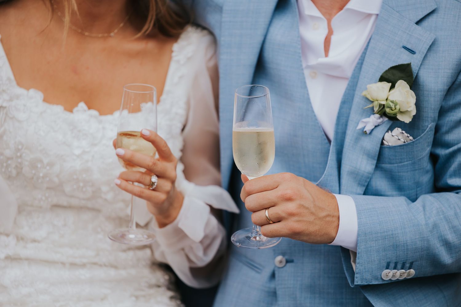 A group of wedding guests holding champagne glasses together in a celebratory toast while wearing light blue suits.