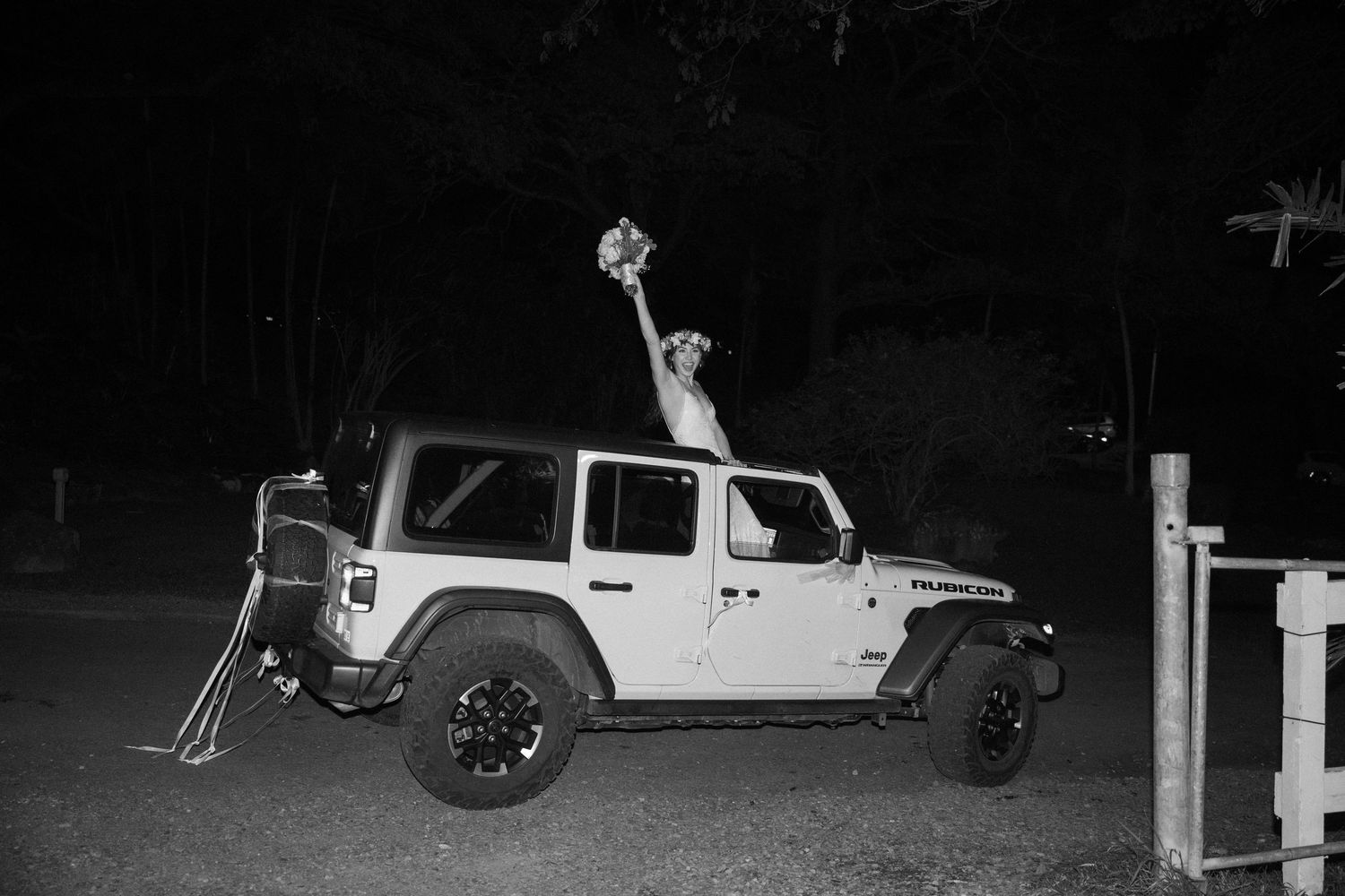 White Jeep Wrangler parked at night with celebratory pose through sunroof.