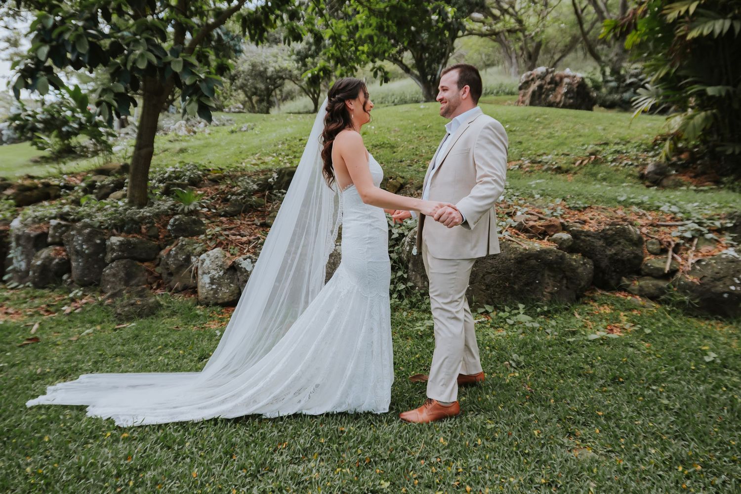 Couple in white and beige attire having their first look moment in a garden setting.