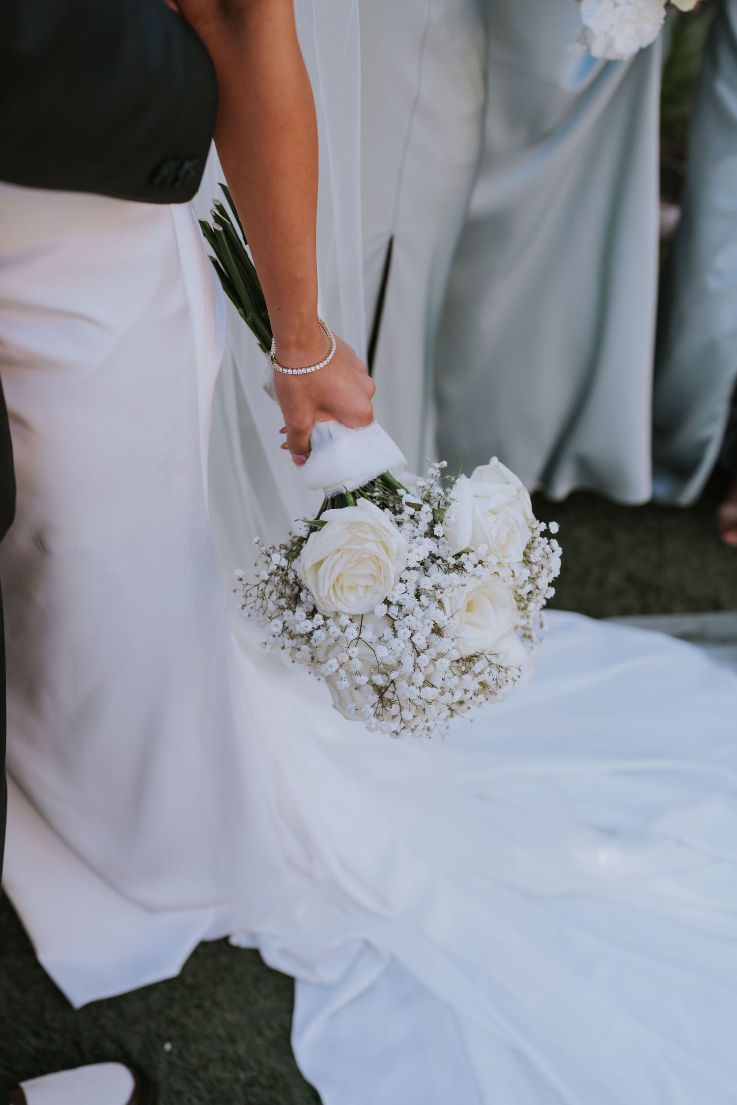 A delicate white rose and baby's breath wedding bouquet held against a flowing white wedding dress.