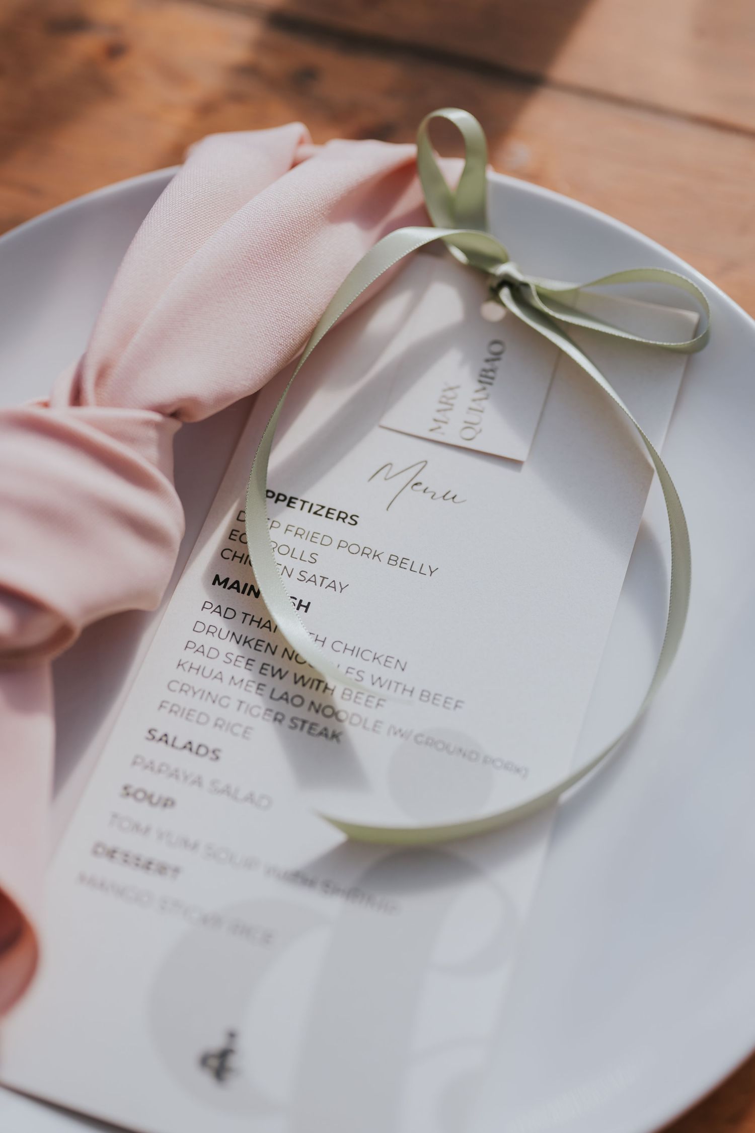 A series of elegant white menu cards with delicate green ribbons displayed on a light wooden surface.