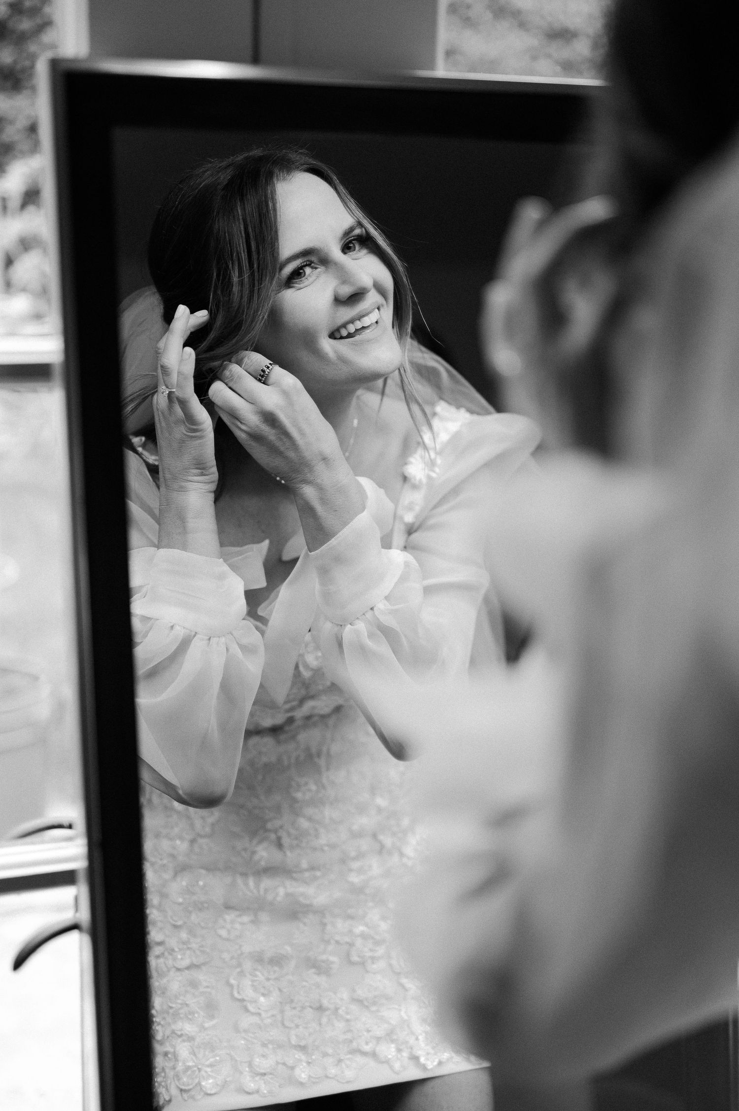 Black and white reflection in mirror shows someone in a white shirt smiling and touching their hair.
