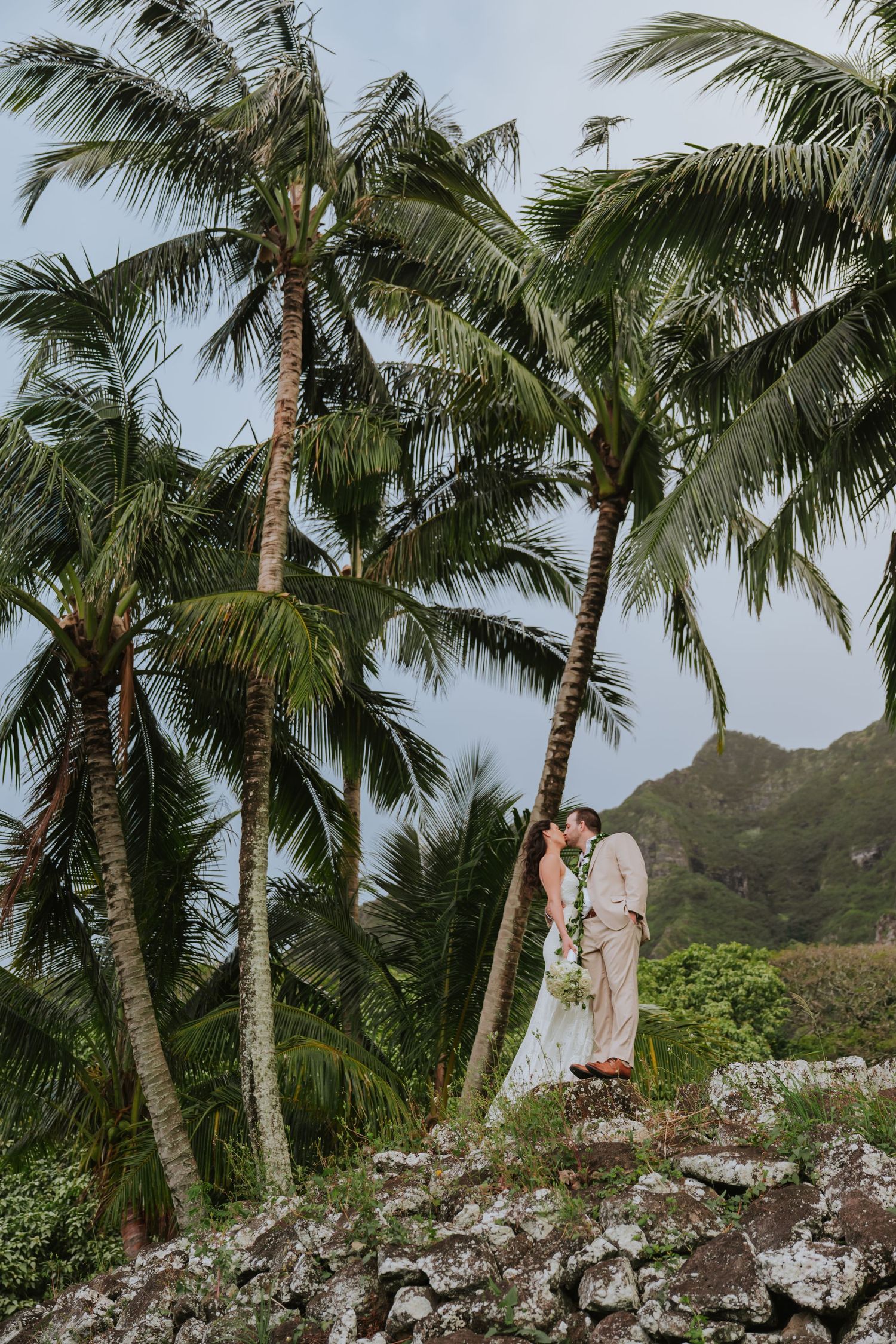 Couple walking among tall palm trees on a rocky tropical hillside path in Hawaii.