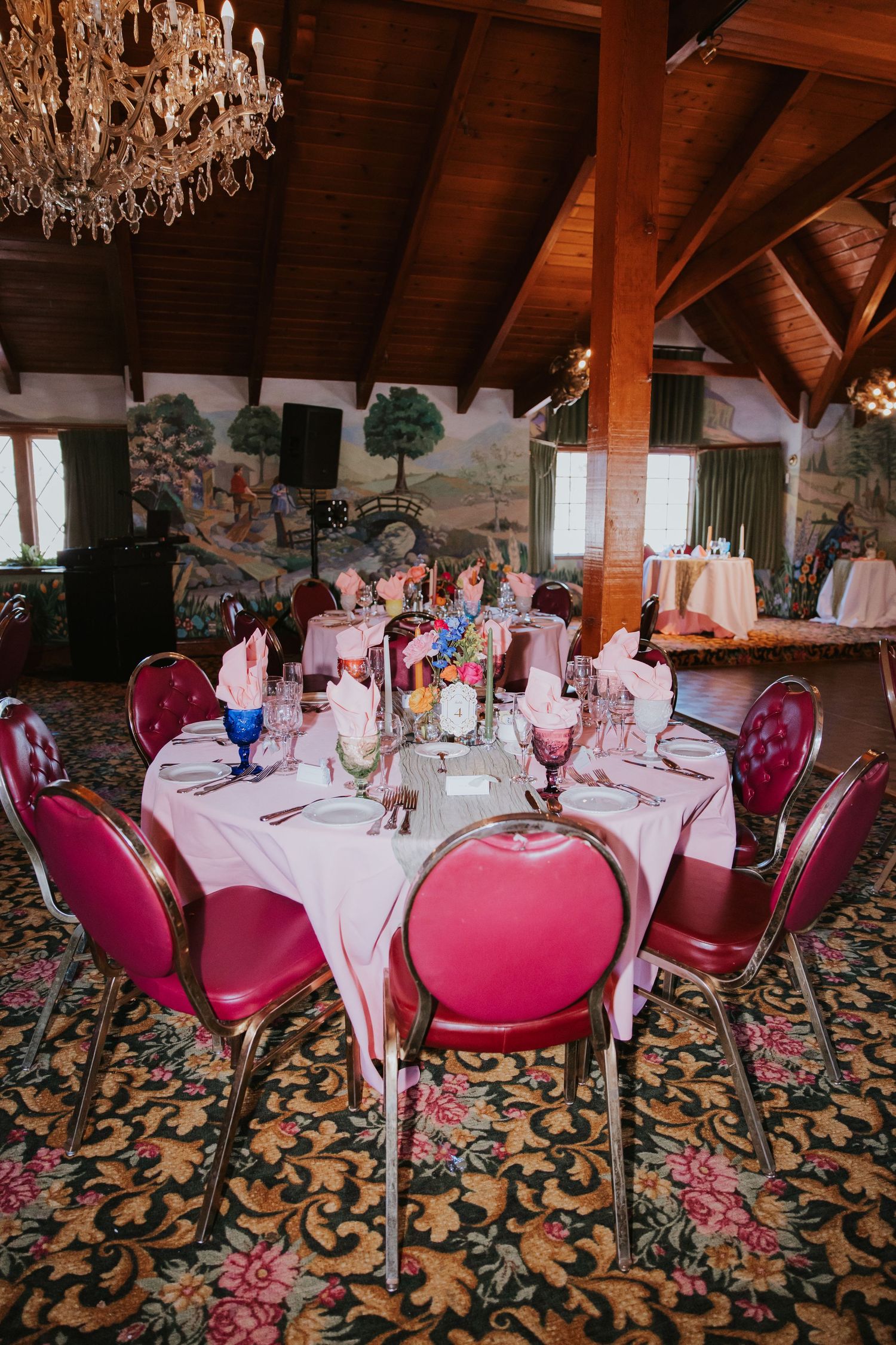 Elegant dining room with crystal chandeliers, burgundy velvet chairs and floral patterned carpet set for formal dinner service.