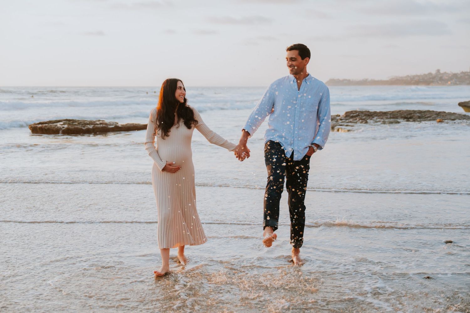 Playful couple splashing and walking in ocean waves at beach.