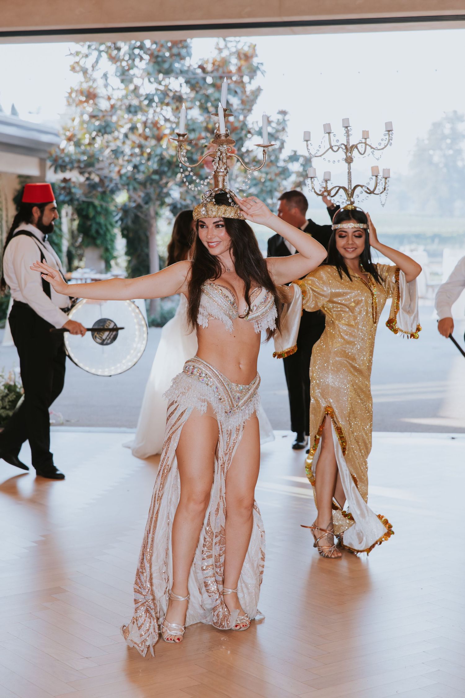 Belly dancers in ornate costumes balance candelabras on their heads at an elegant event.