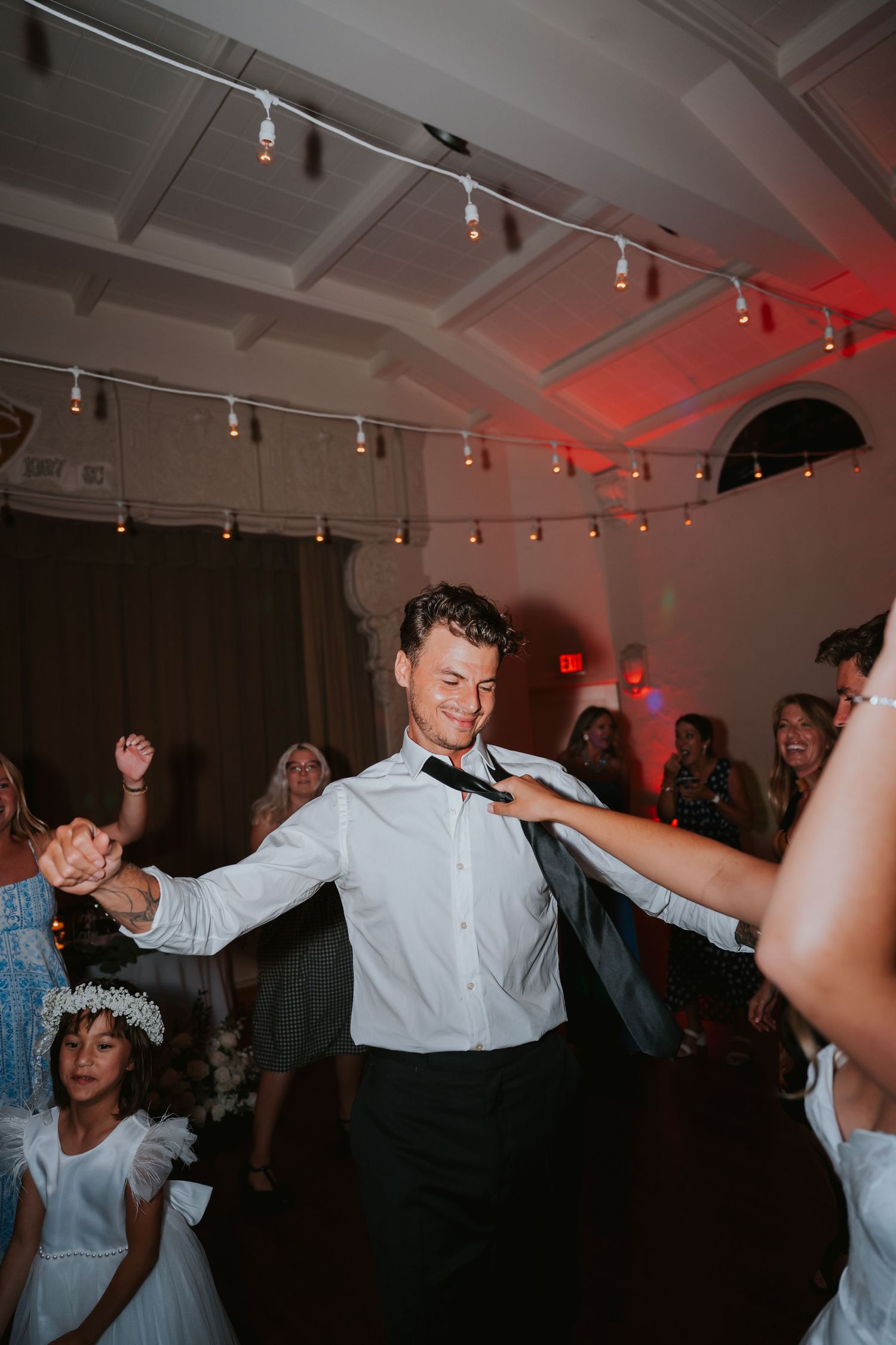 People dancing and celebrating at a wedding reception with track lighting and white ceiling decor.