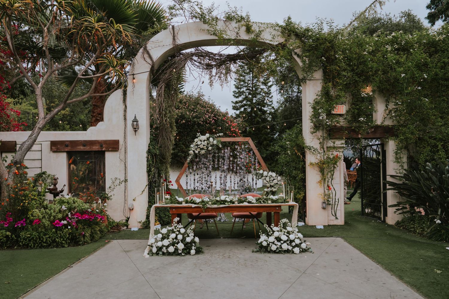 Wedding venue exterior showing white buildings and garden pathways decorated with floral arrangements.