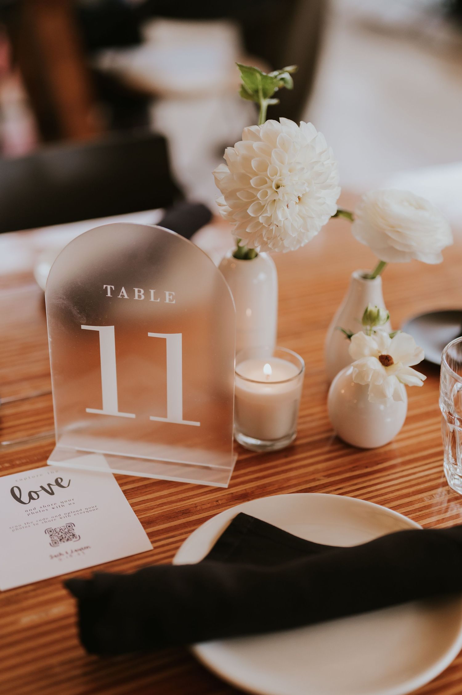White table number and floral decor with candles create an elegant wedding reception centerpiece on a wooden table.