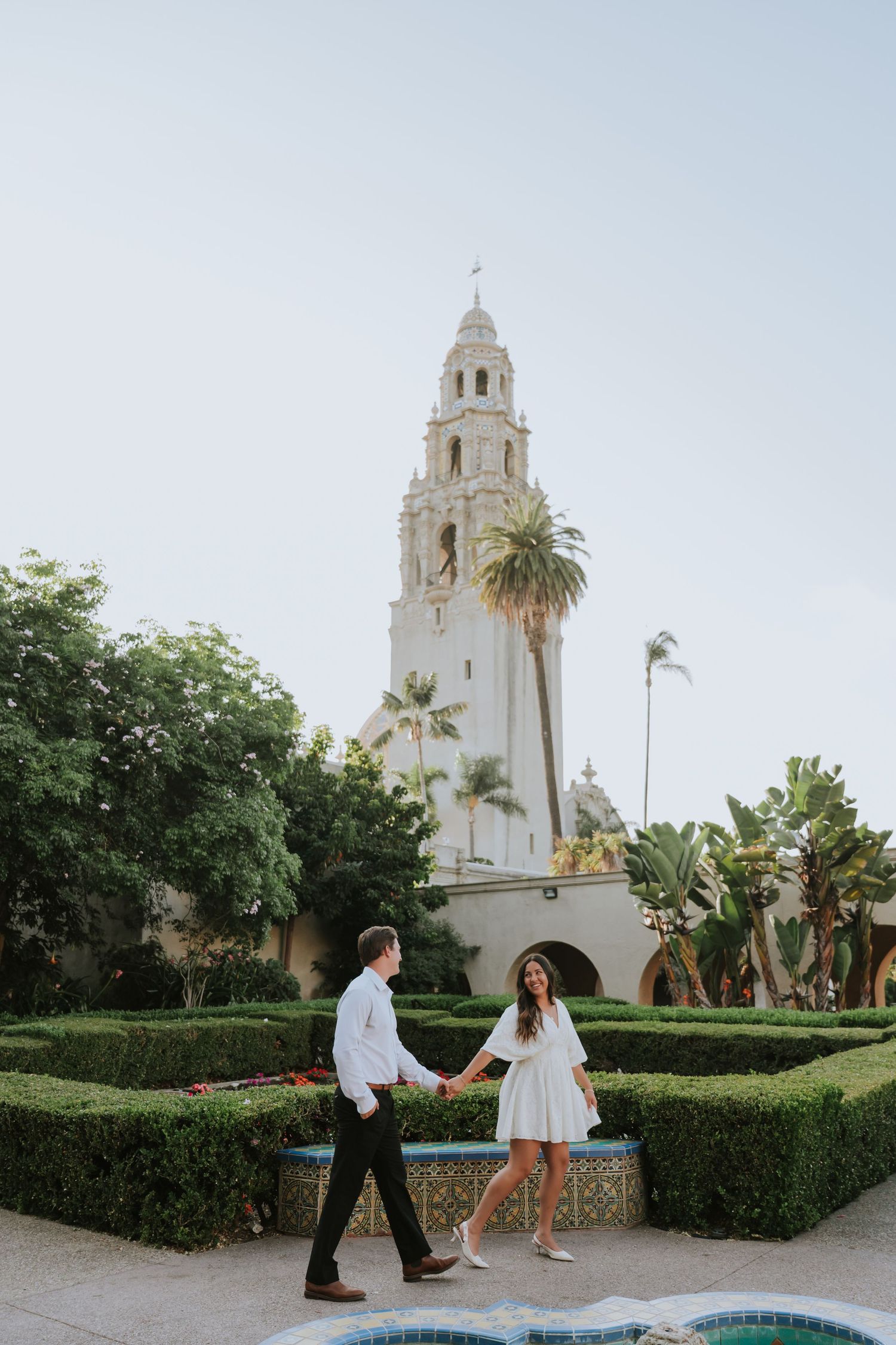 Marriage proposal in front of a Spanish colonial style church with white towers and palm trees.