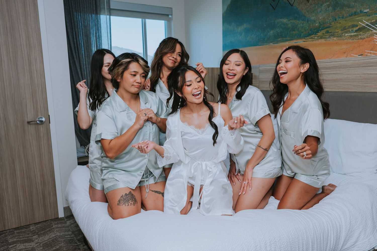 A group of friends in white clothing laughing and having fun together on a bed.