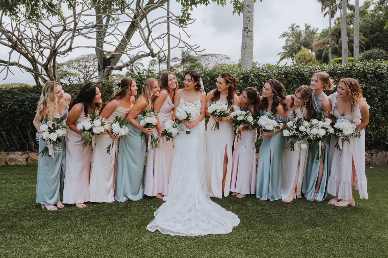 A row of bridesmaids in pastel pink and blue dresses pose together at an outdoor wedding ceremony.