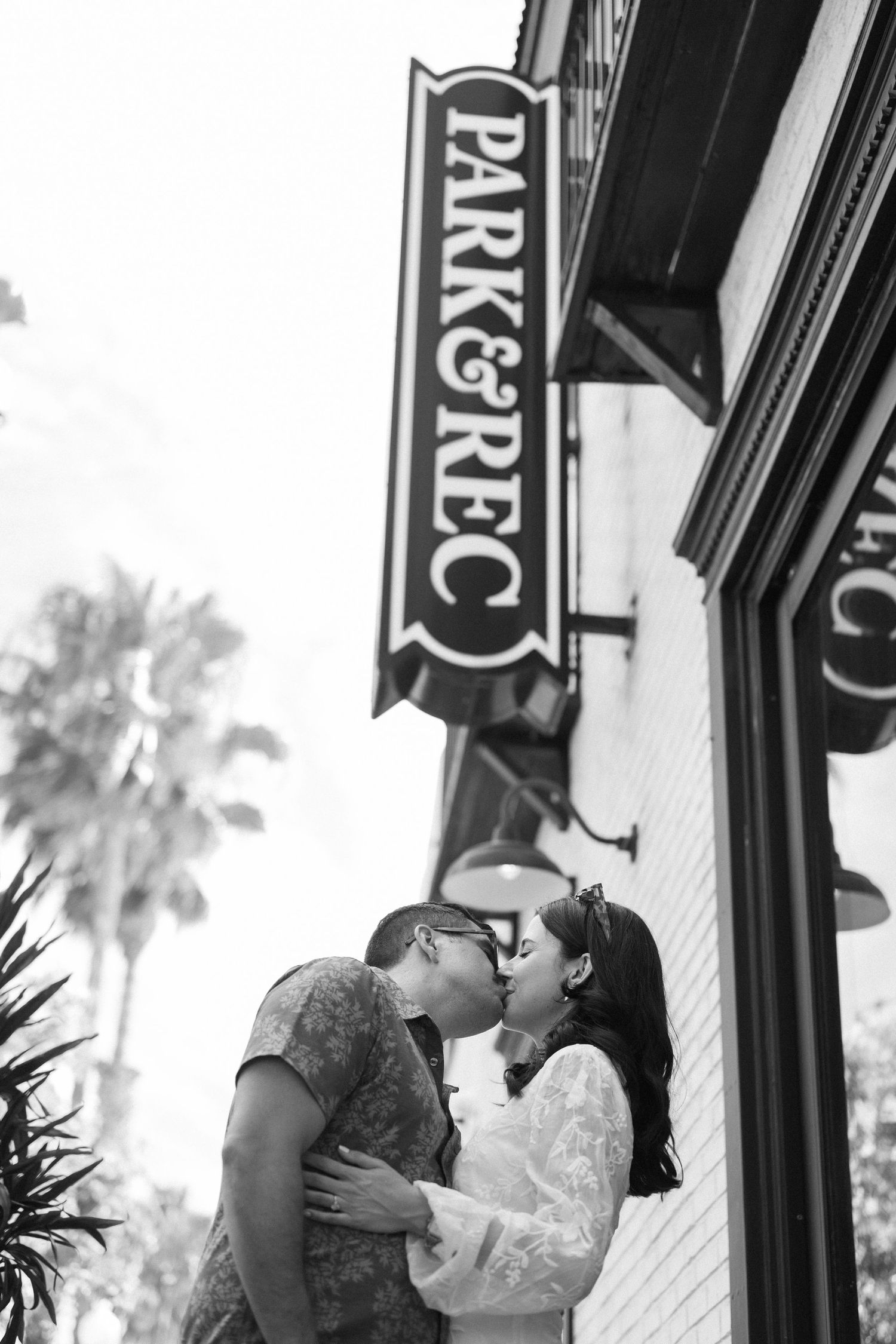 A romantic black and white photo series showing a couple embracing and kissing against a storefront exterior.