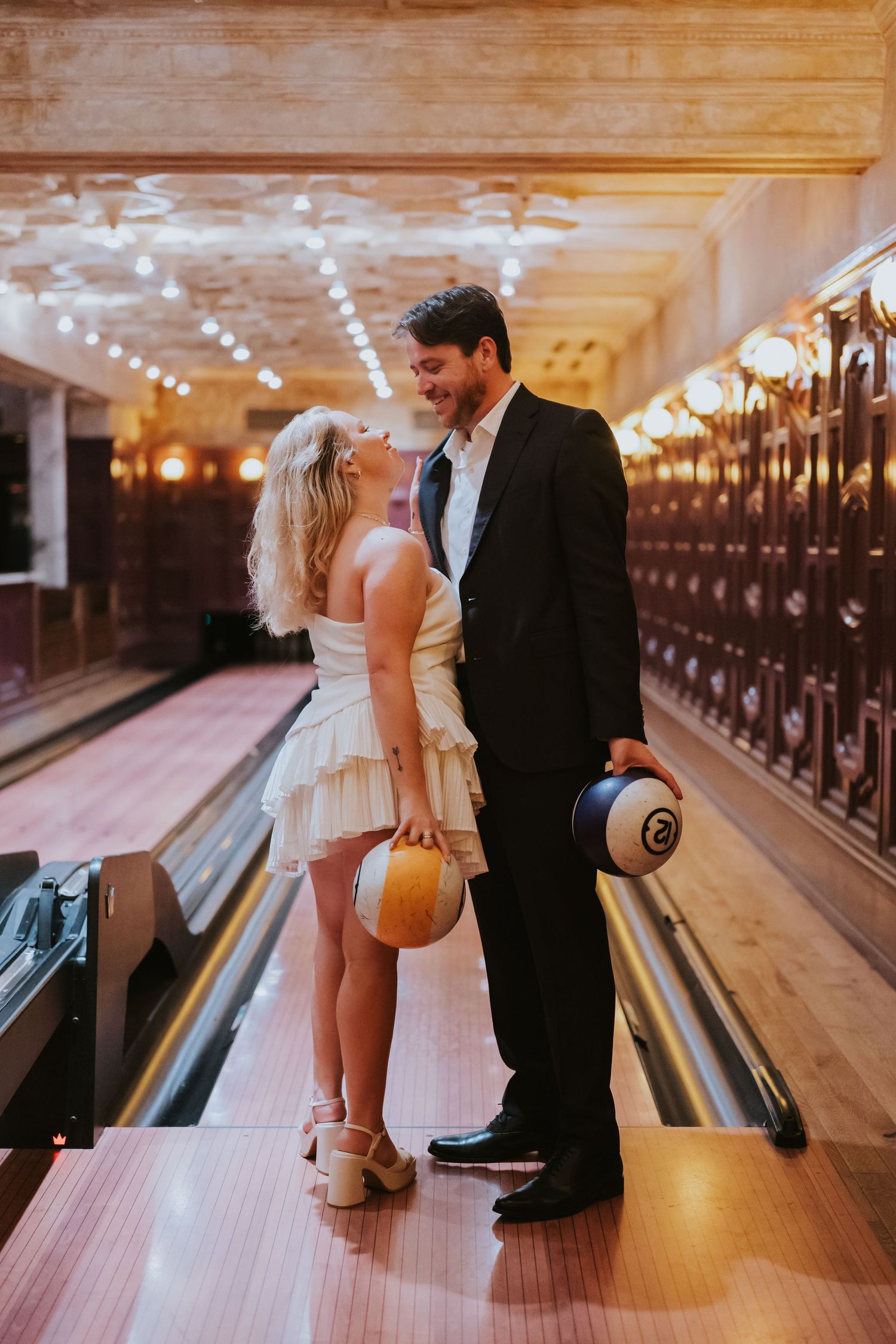 Bride and groom sharing a romantic moment on a vintage bowling alley lane holding bowling balls.