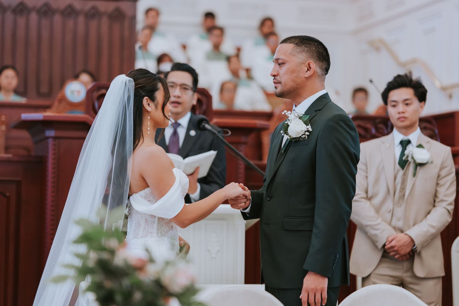 A couple exchanges vows during their wedding ceremony in a traditional church setting with bridesmaids and groomsmen present.