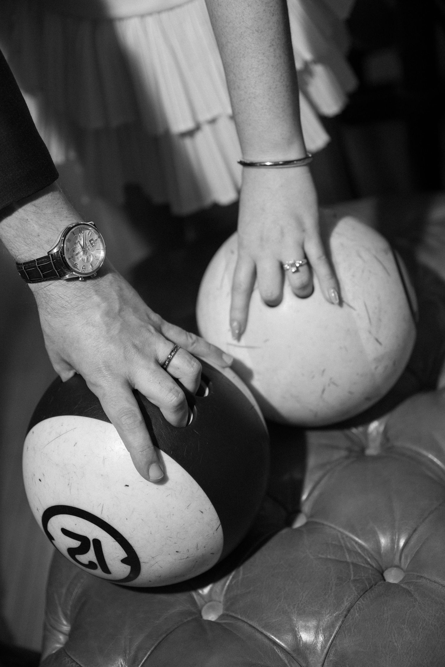 Black and white close-up of bride and groom hands with wedding rings resting on billiard balls.