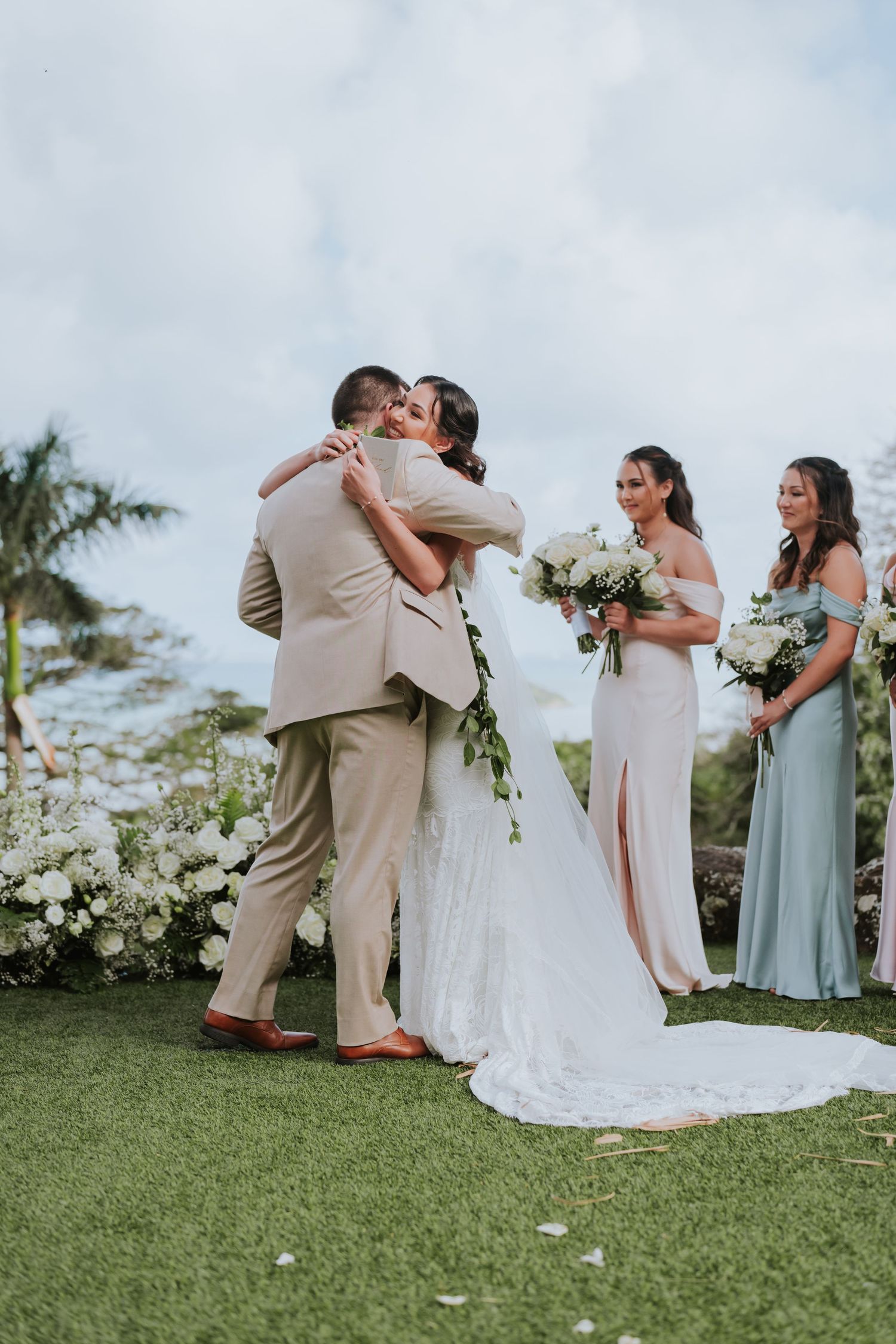 Wedding party stands on a grassy hill during an outdoor ceremony with bridesmaids in sage green dresses.