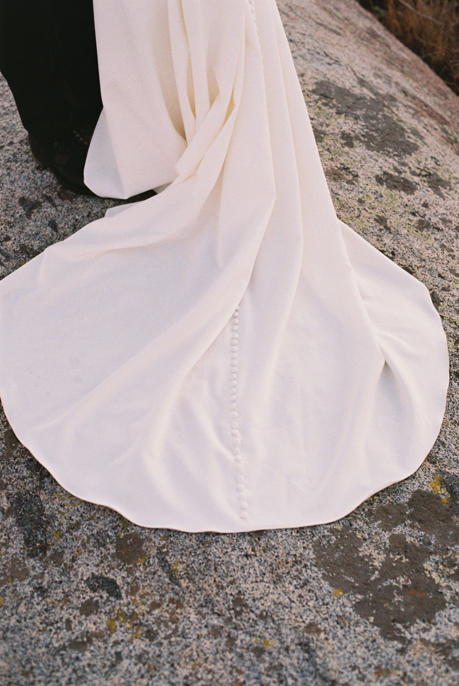 Elegant white wedding dress train spread on stone ground, showcasing intricate seam detail and flowing silhouette.