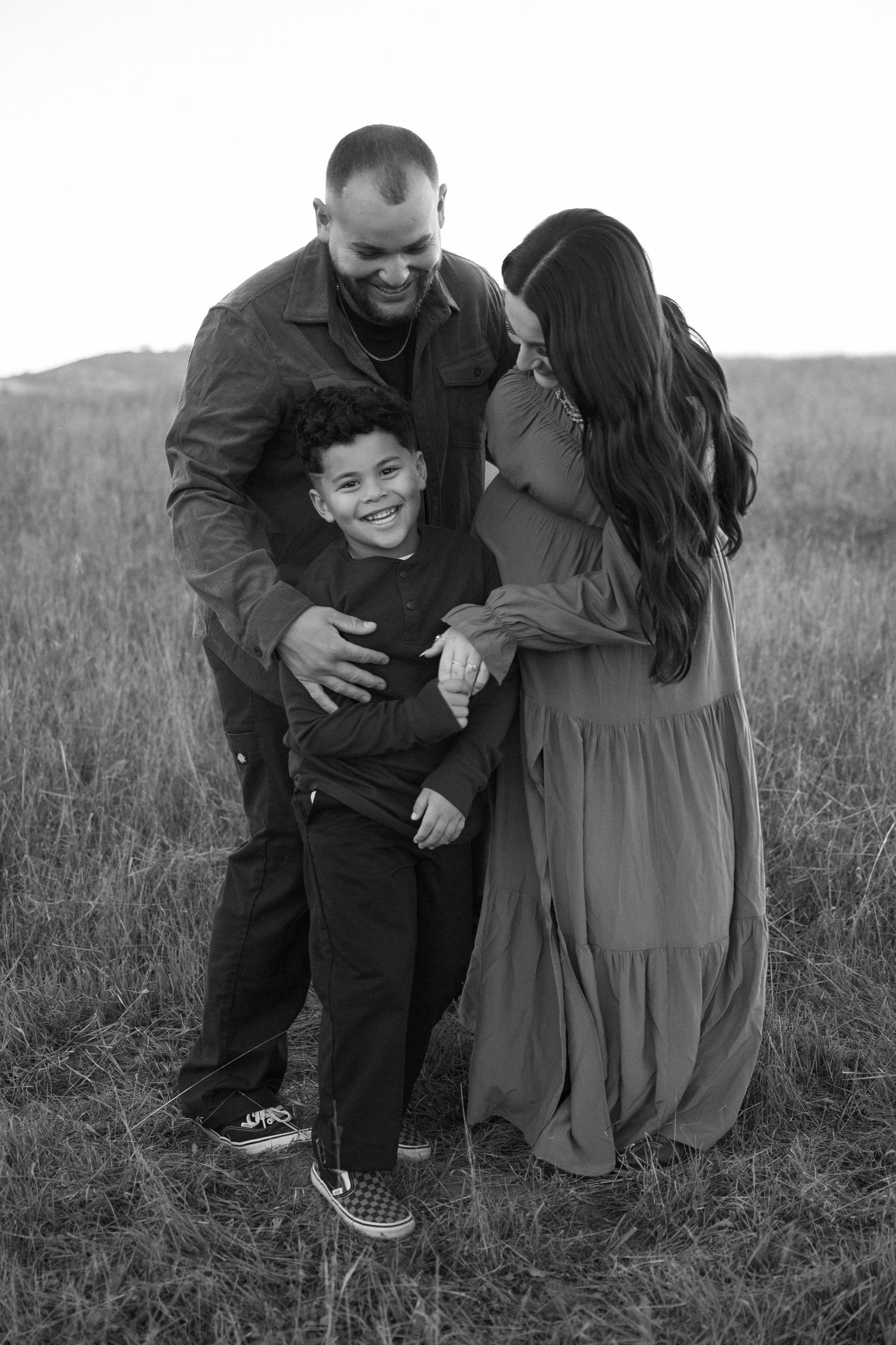 A couple shares a joyful moment together in a grassy field wearing casual attire in black and white photography.