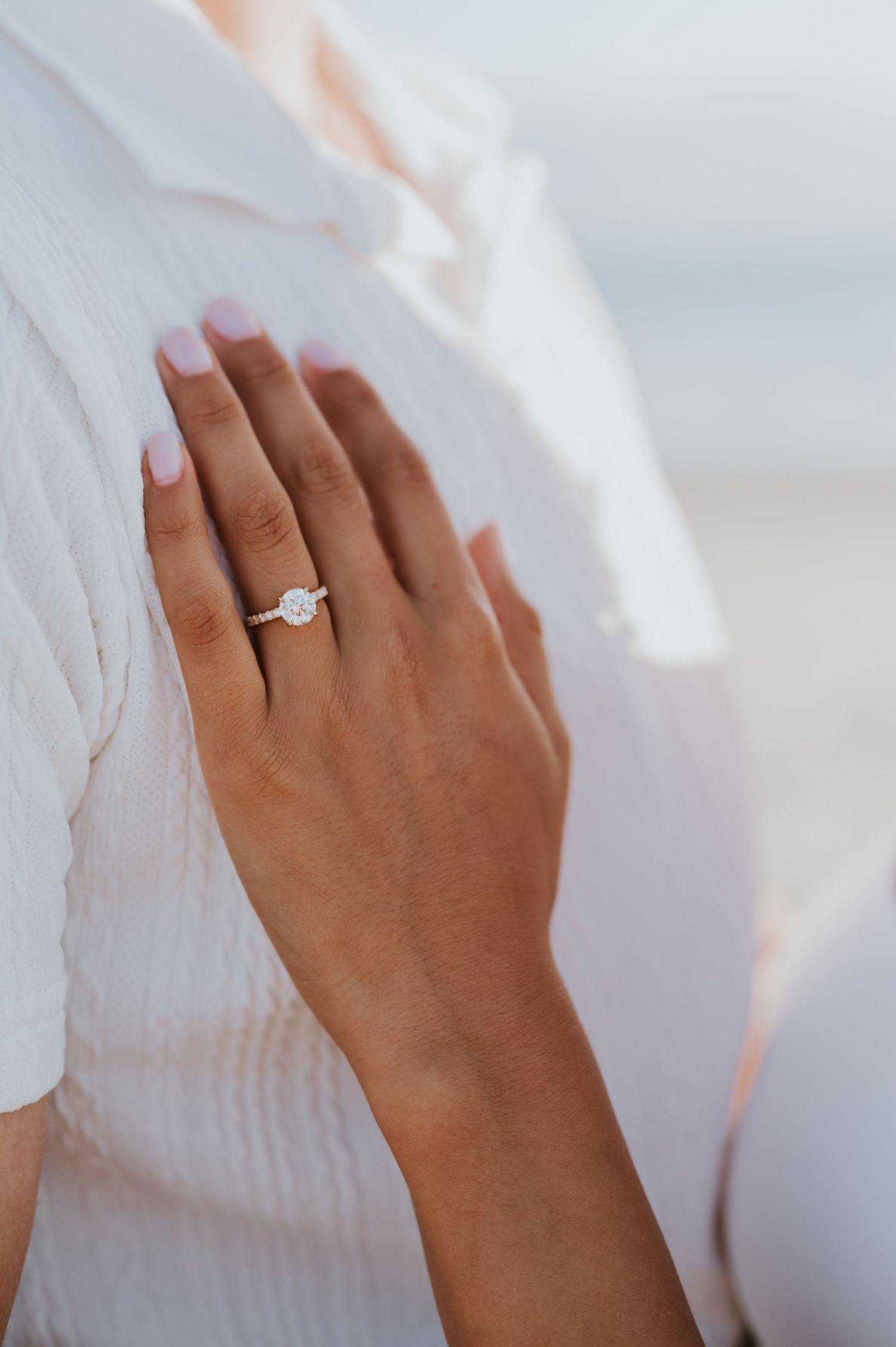 Hand wearing a solitaire diamond engagement ring against a soft white fabric background.