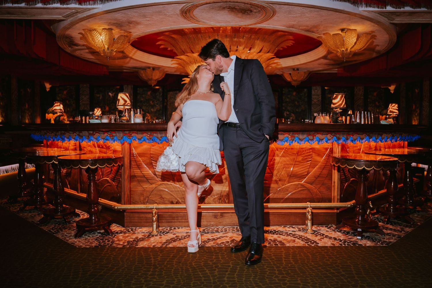 Couple sharing a romantic kiss in an elegant bar venue with ornate gold decor and warm lighting.