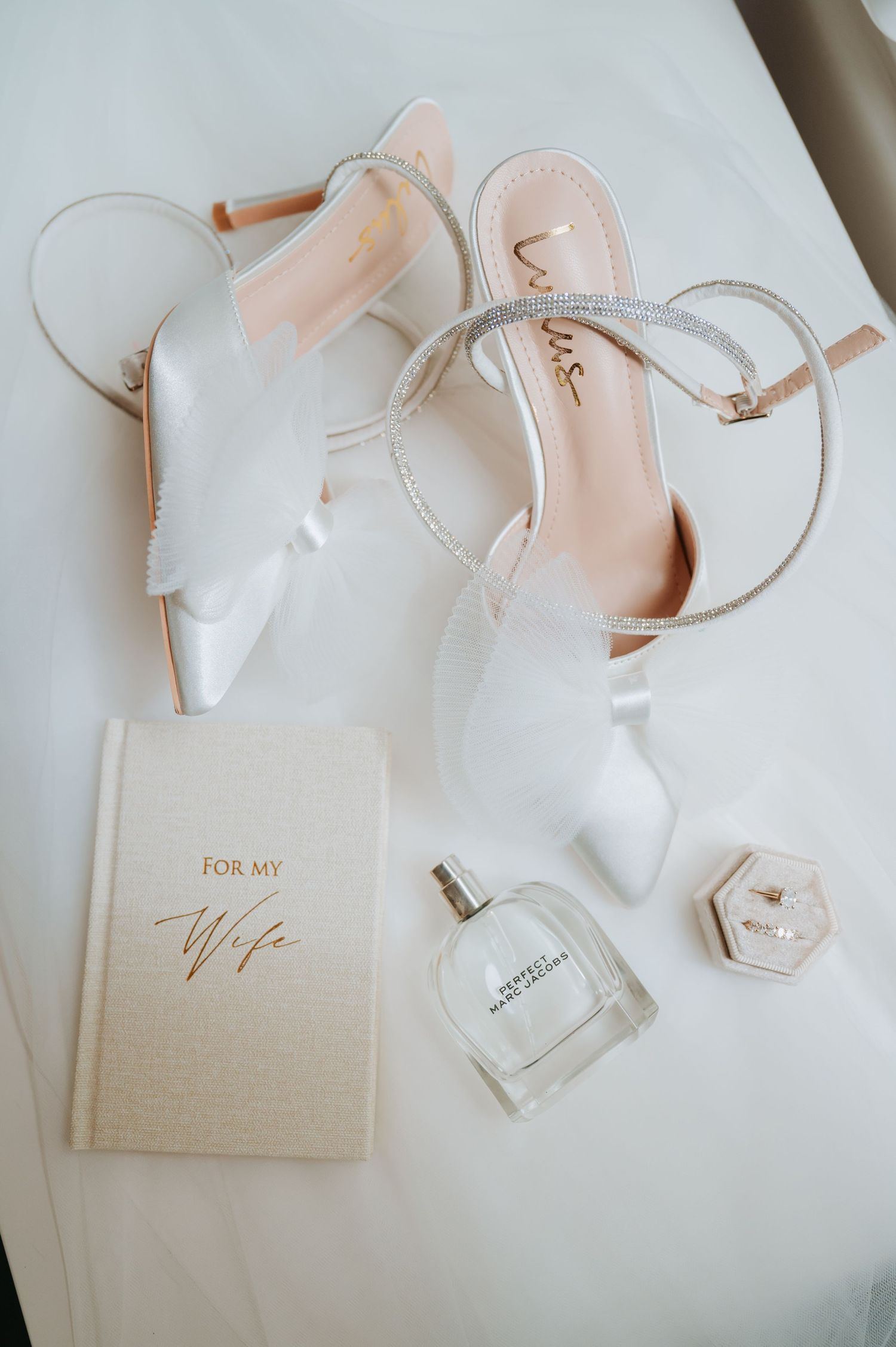 Bridal accessories including blush heels and wedding stationery arranged on white background.