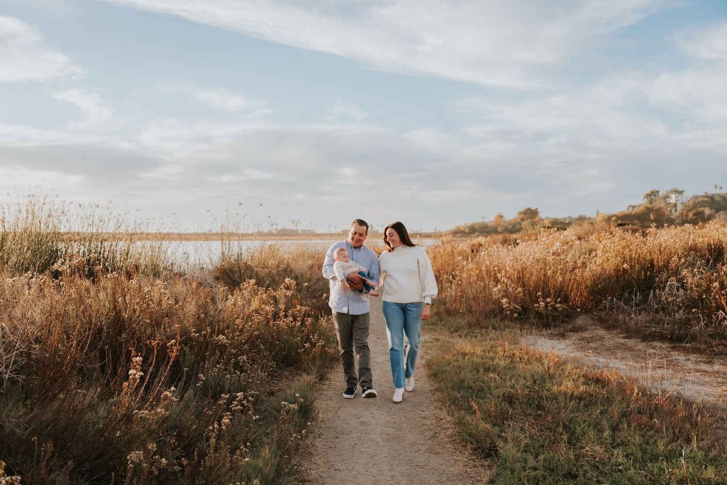 Family walking together on nature trail at sunset near water.