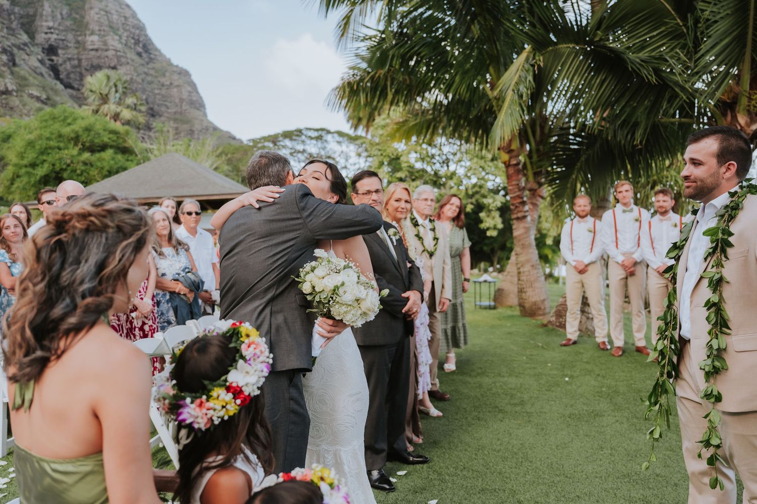 Wedding celebration with guests lined up outdoors against dramatic mountain backdrop in Hawaii.