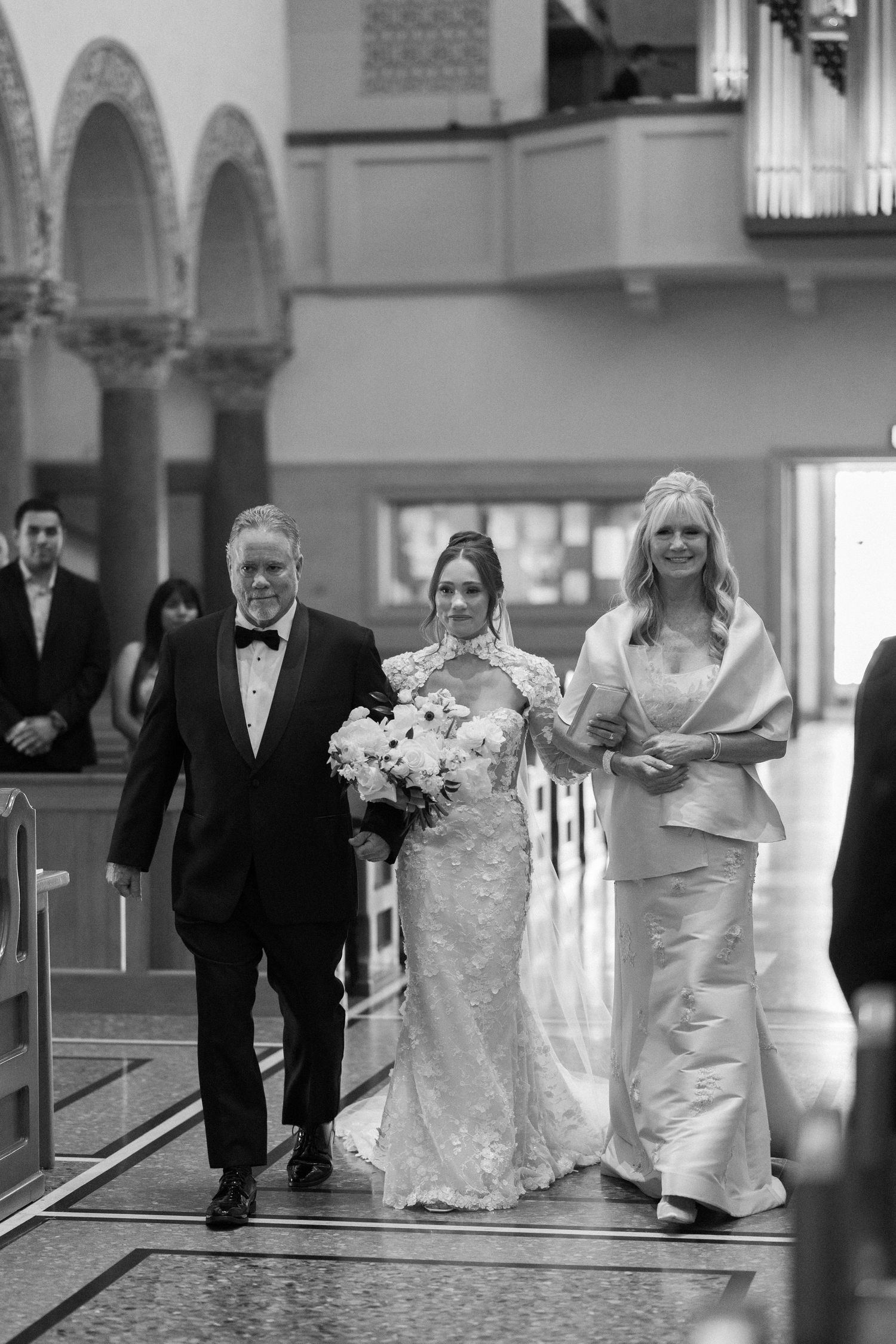 Black and white photo of a wedding party walking through church pews.