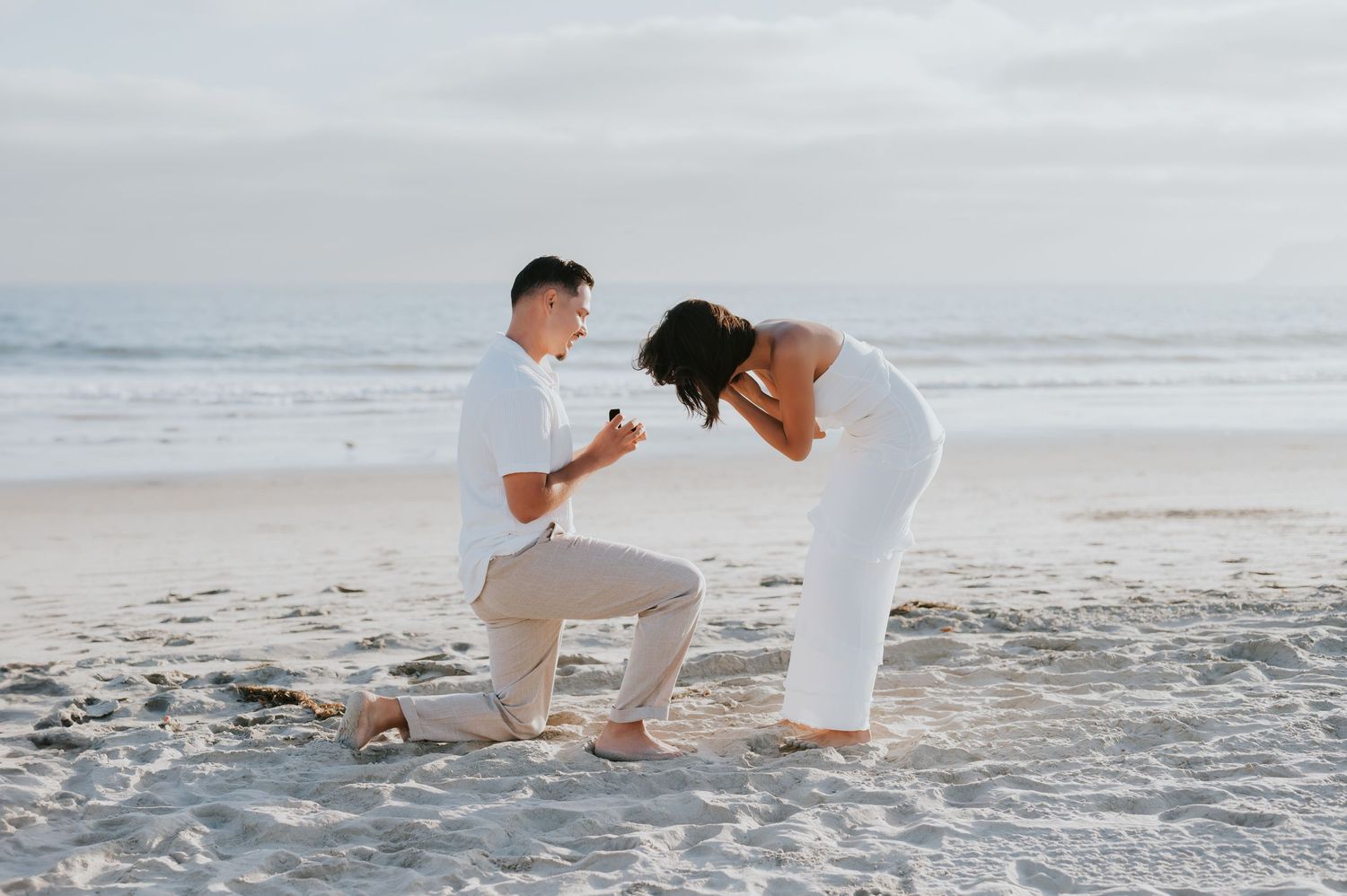 A romantic proposal scene unfolds on a misty beach with waves rolling in the background.