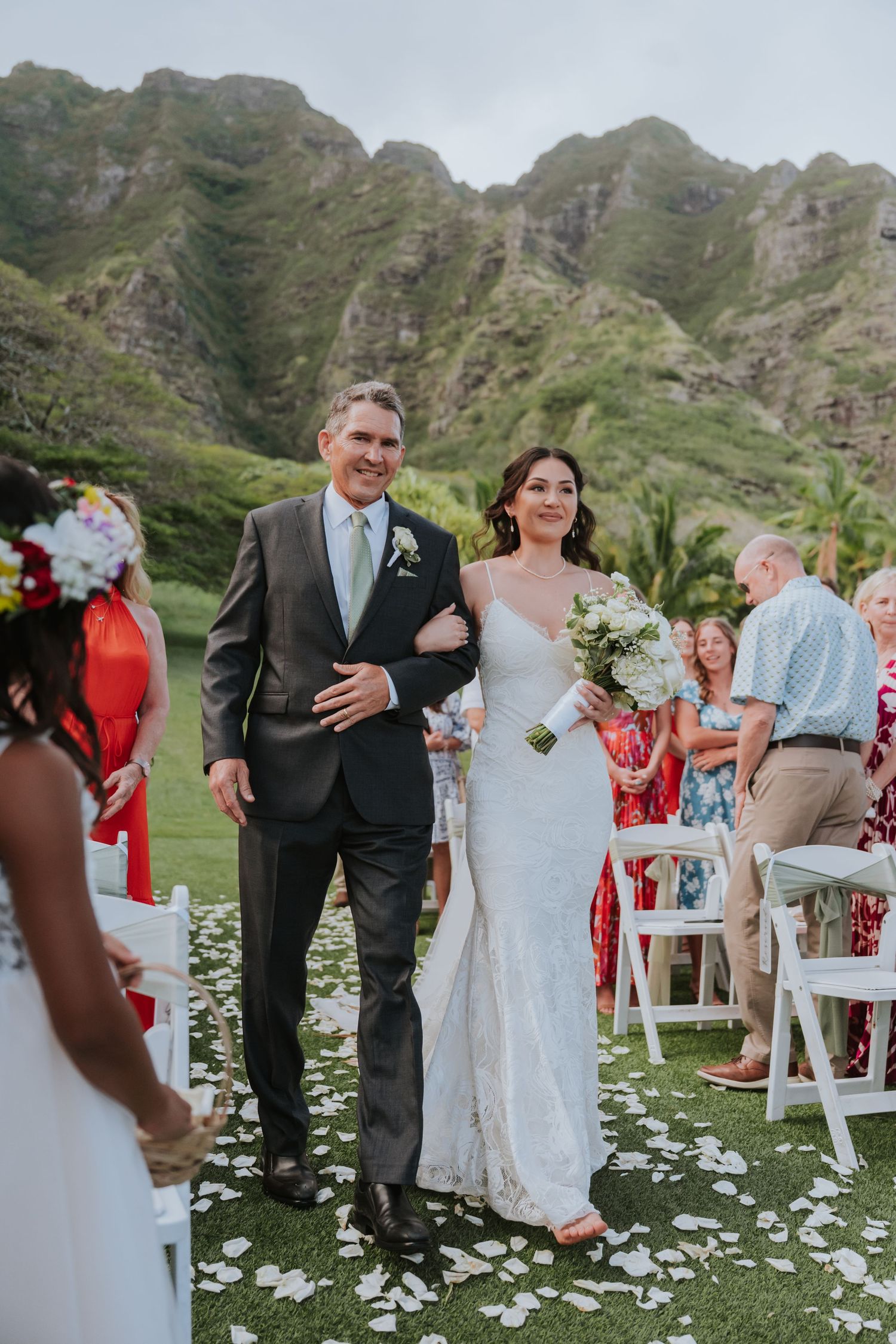 Outdoor wedding ceremony in a lush mountain valley with white flower petals scattered along the aisle.