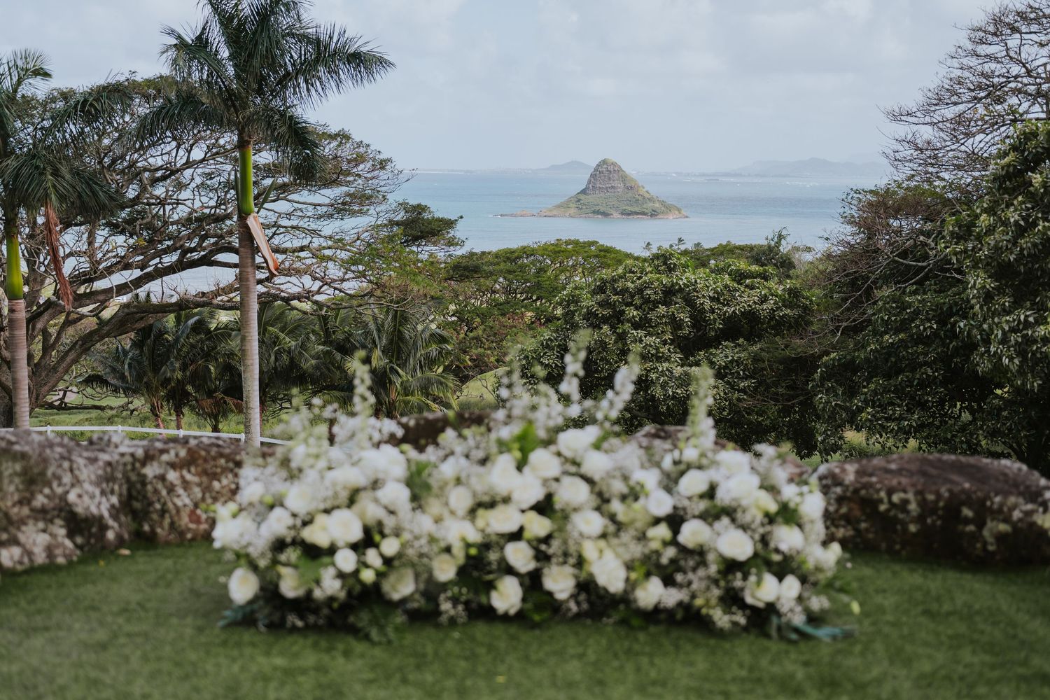 White floral arrangement decorates an outdoor garden with Chinaman's Hat island visible in the distance off Oahu's coast.