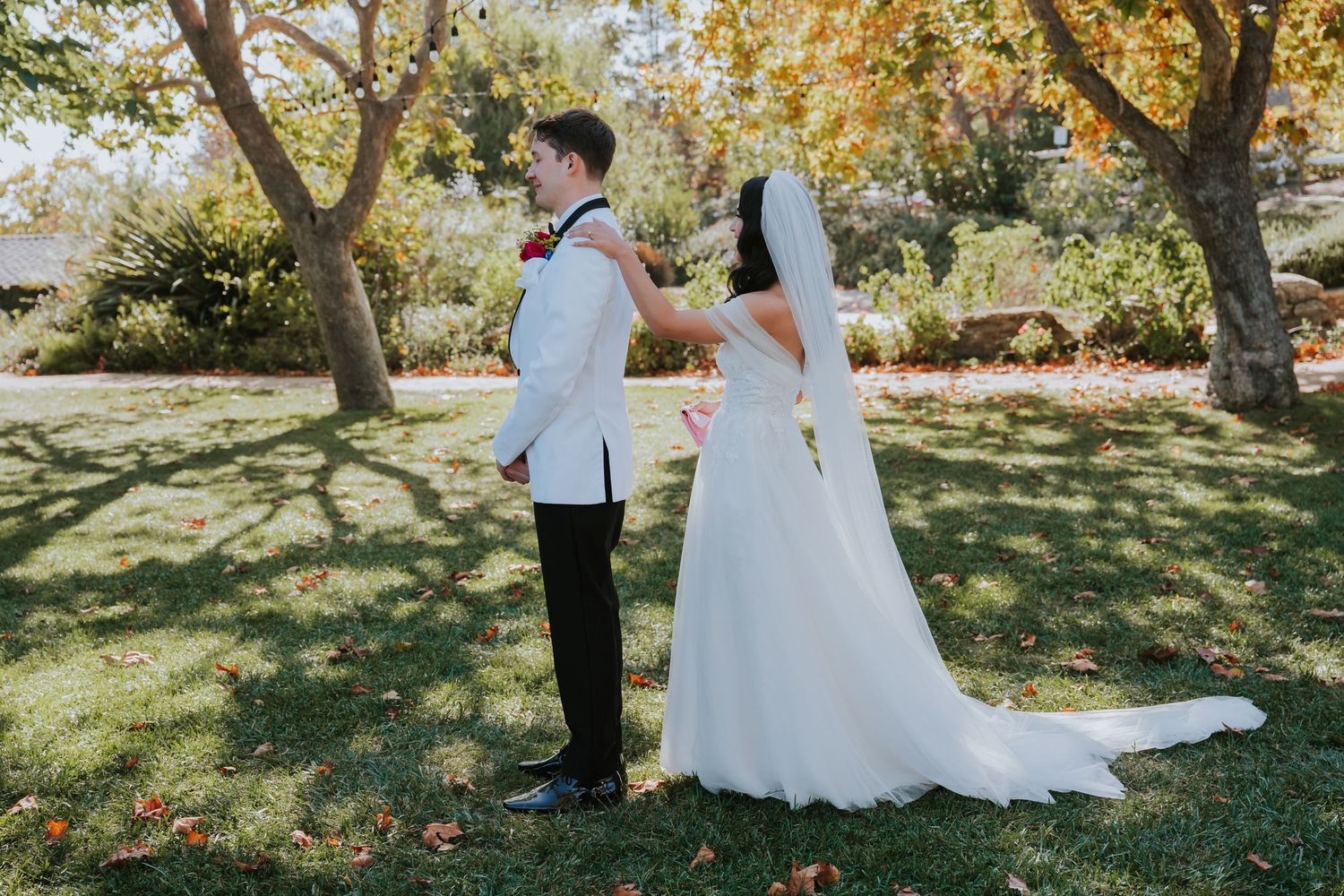 Wedding couple poses in sunlit autumn garden with fallen leaves.
