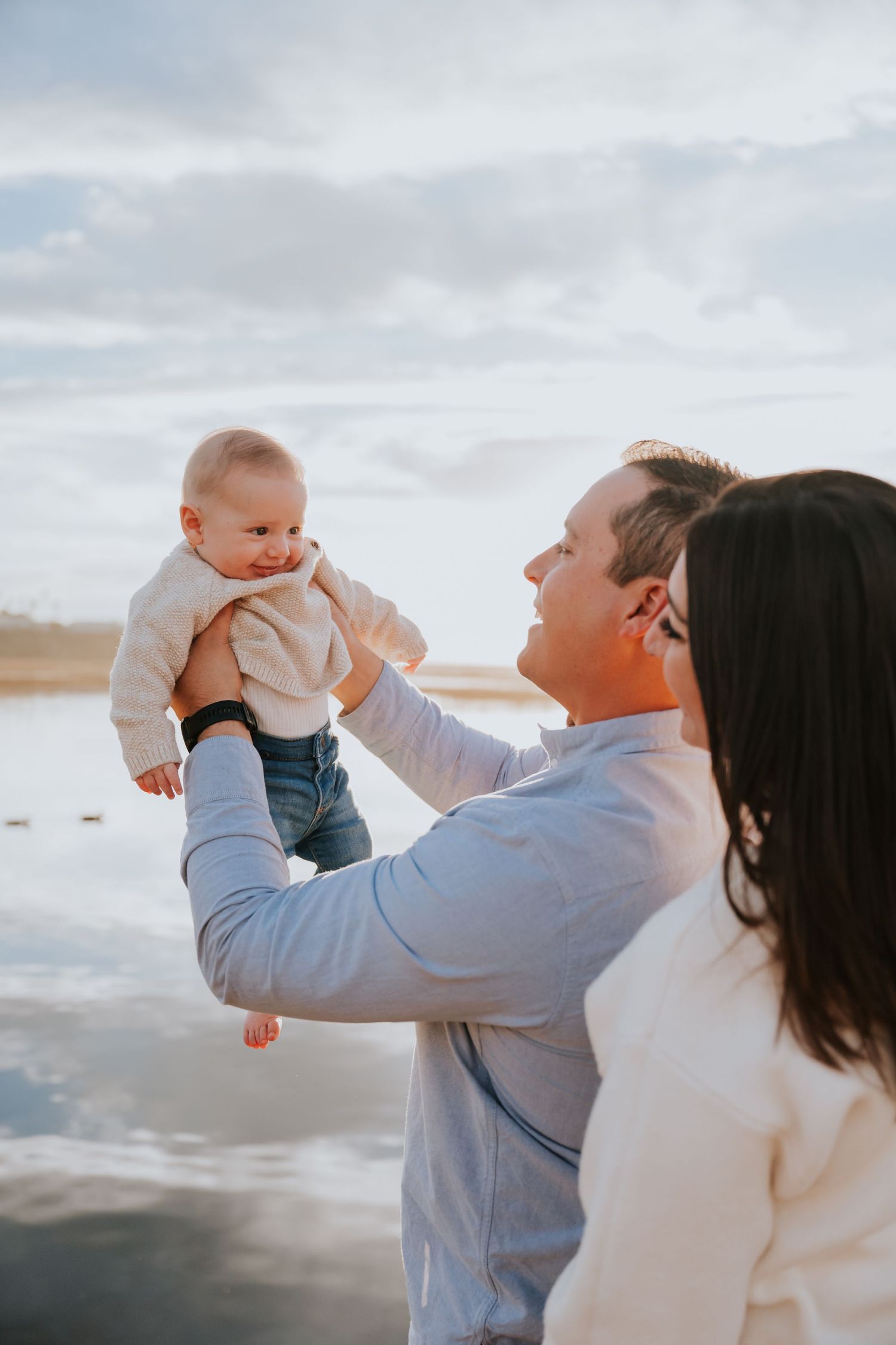 Family enjoying playful moment together at beach during golden hour.