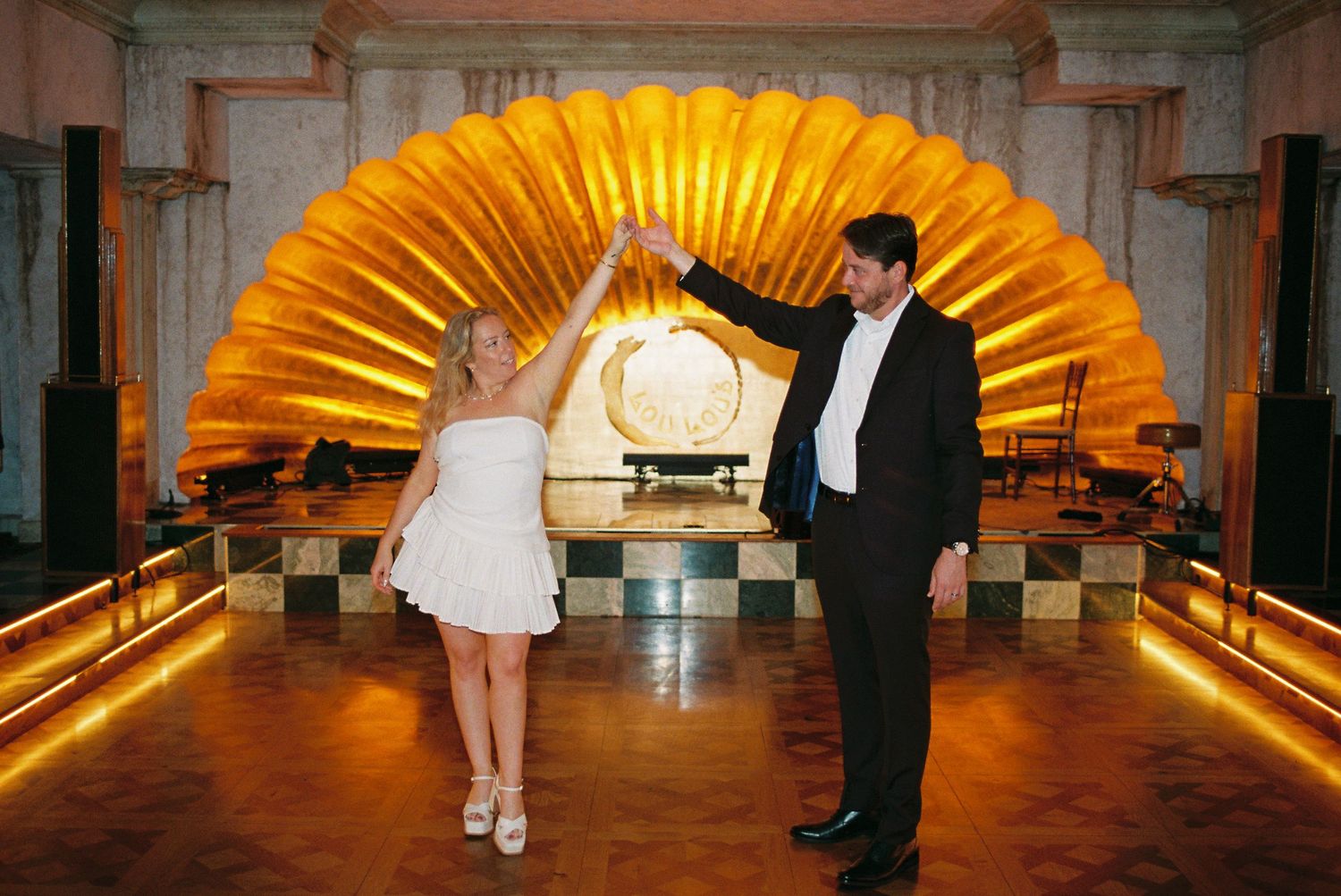 Couple dancing elegantly in front of a stunning golden shell backdrop in an ornate venue.