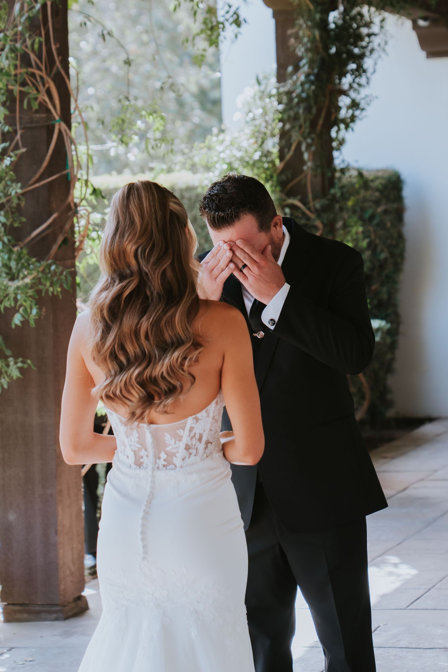 Emotional groom covering his face with his hand during first look moment with bride in lace wedding gown.