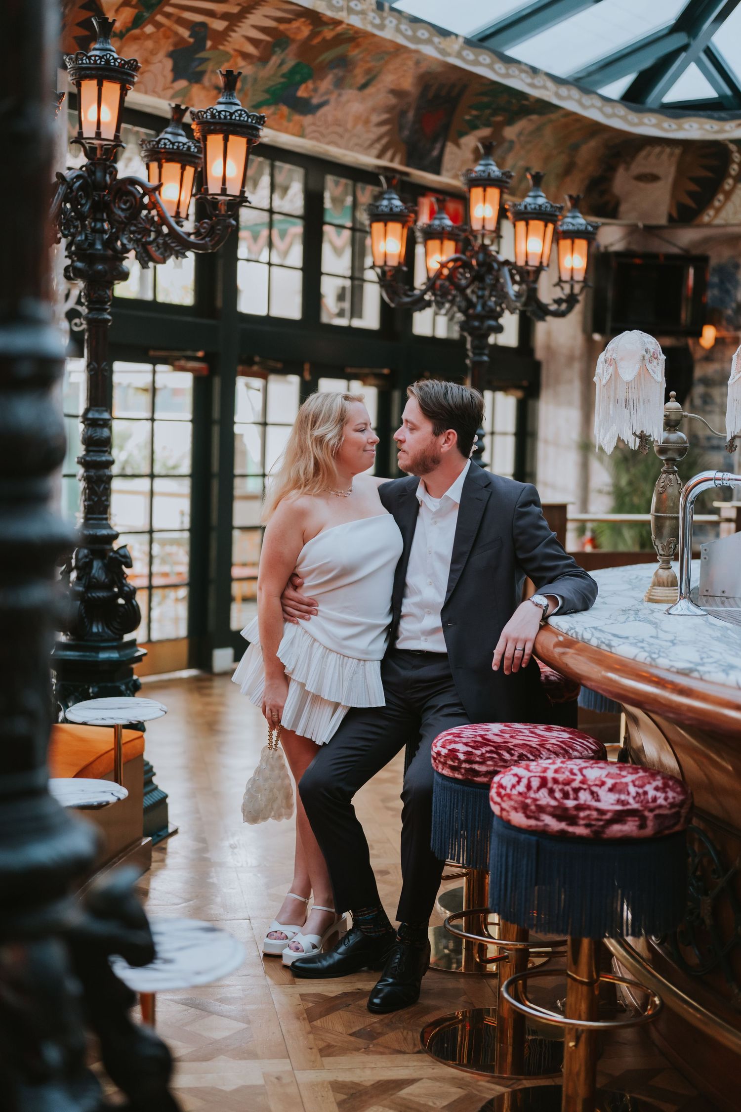 Elegant couple posing at an ornate bar with vintage lanterns in a luxurious restaurant setting.
