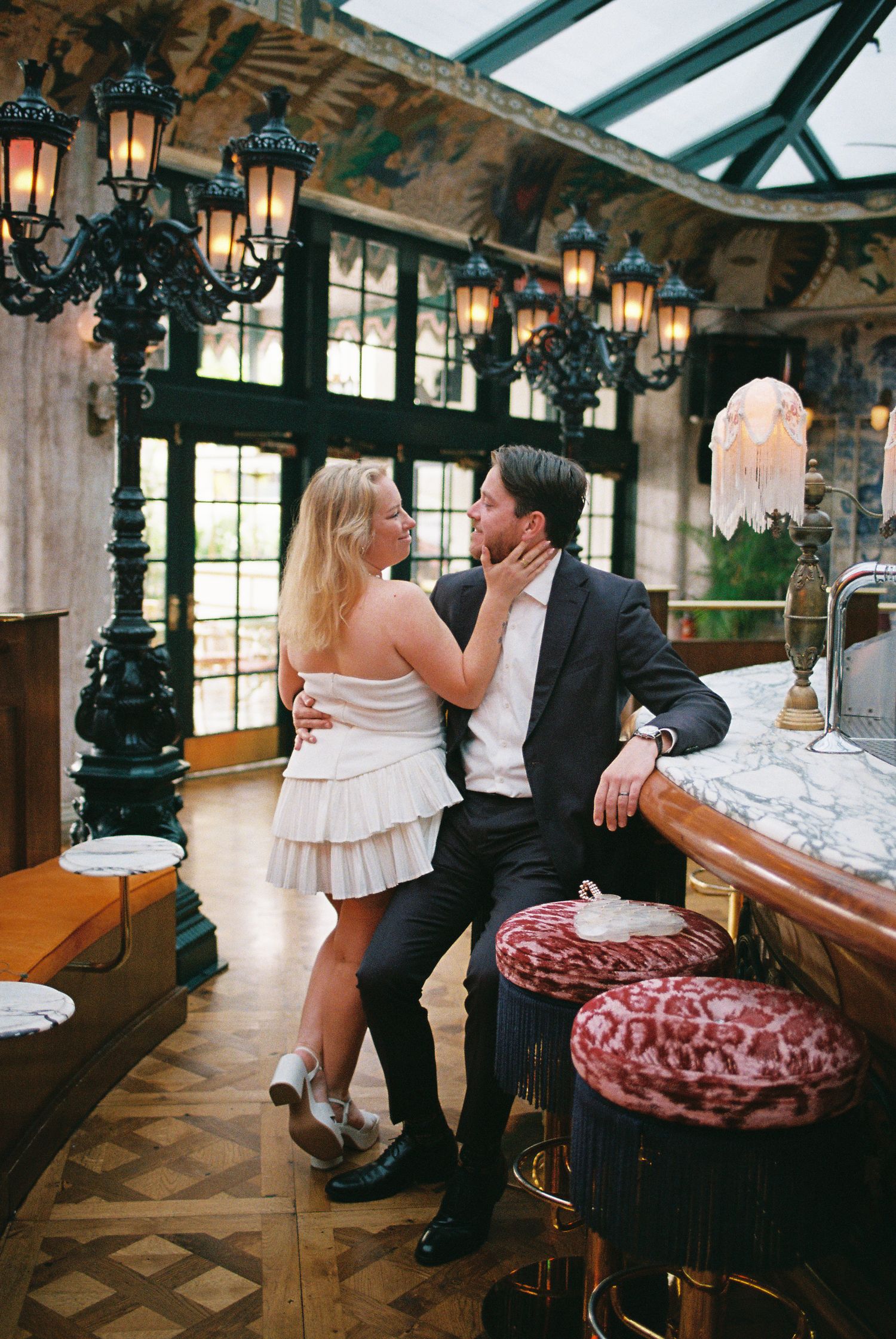 Couple sharing a romantic moment at an elegant bar with ornate lanterns, marble countertop, and leopard print bar stools.
