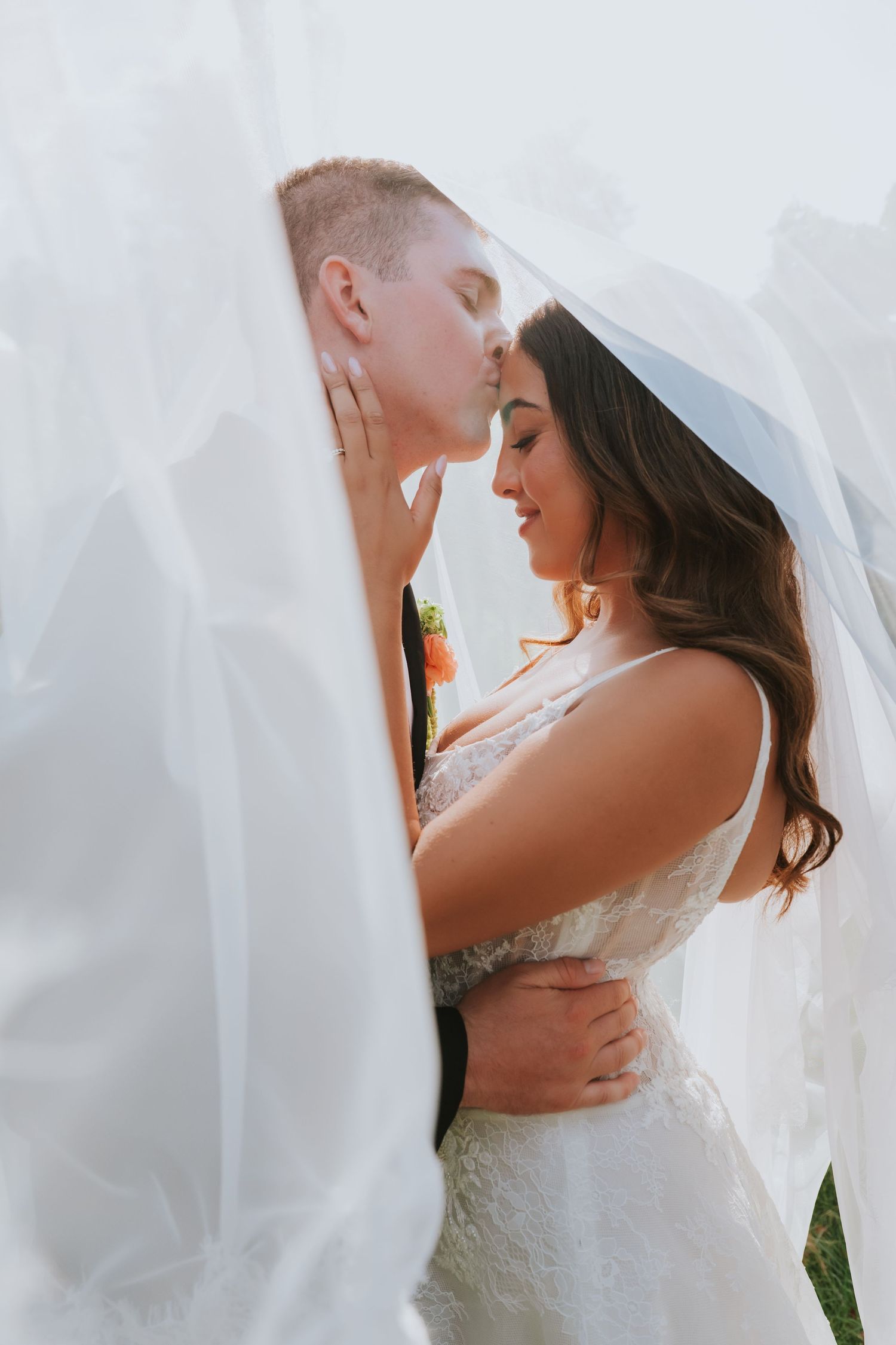 Bride and groom share romantic moment under flowing white veil on wedding day.