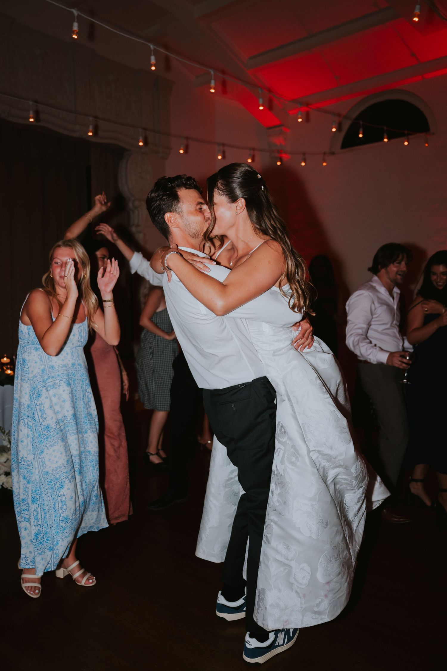Couples dancing together at a dimly lit wedding reception with red ambient lighting creating a romantic atmosphere.