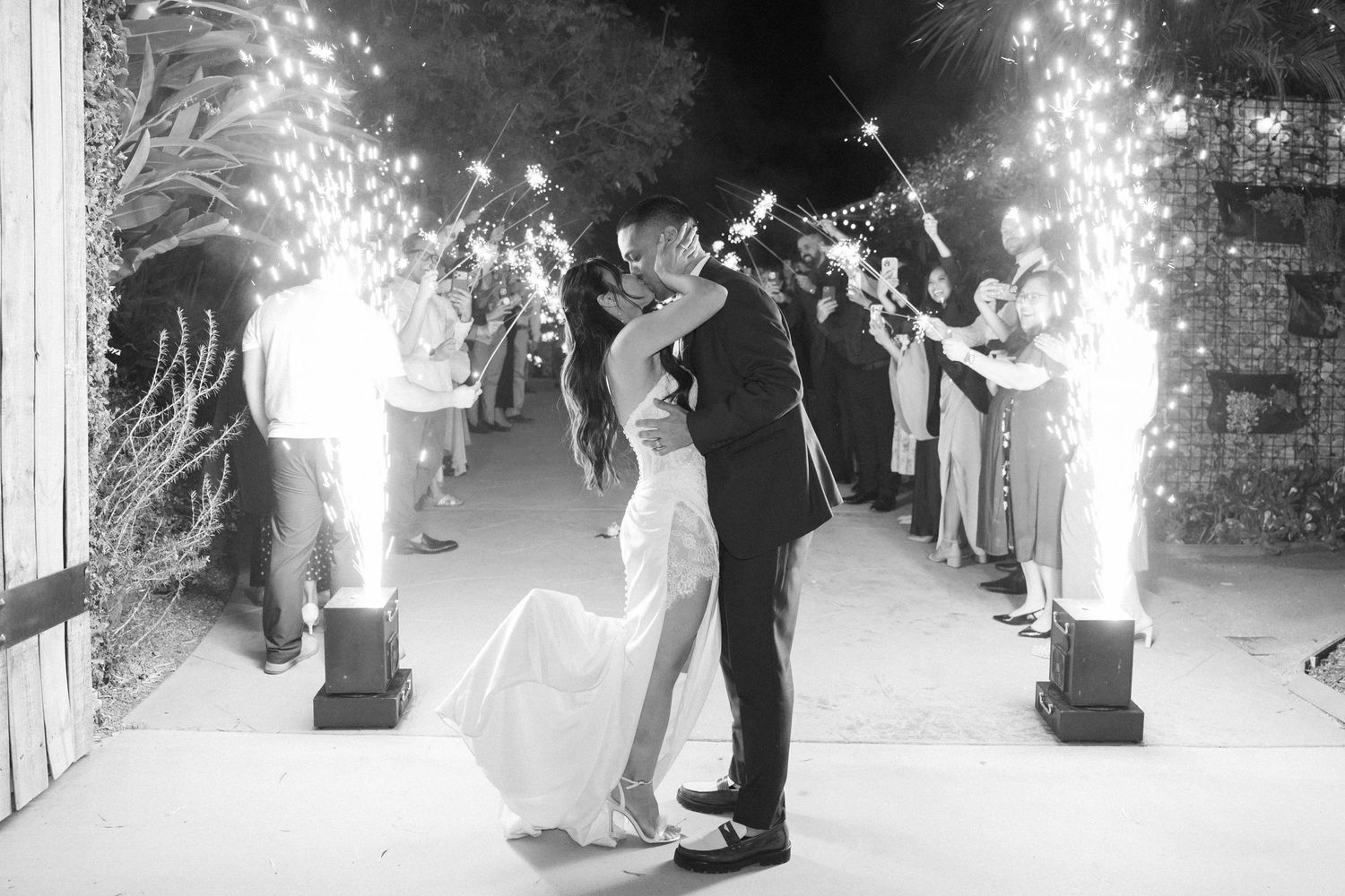 Newlywed couple shares first dance on illuminated dance floor surrounded by sparklers and wedding guests.