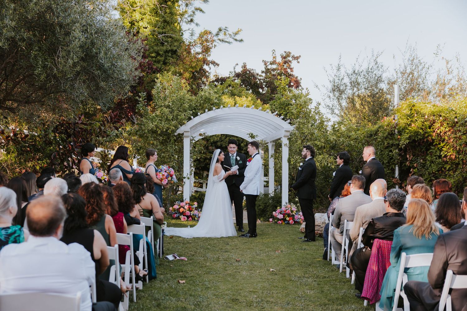 Outdoor wedding ceremony setup with white chairs and gazebo surrounded by autumn trees and natural scenery.