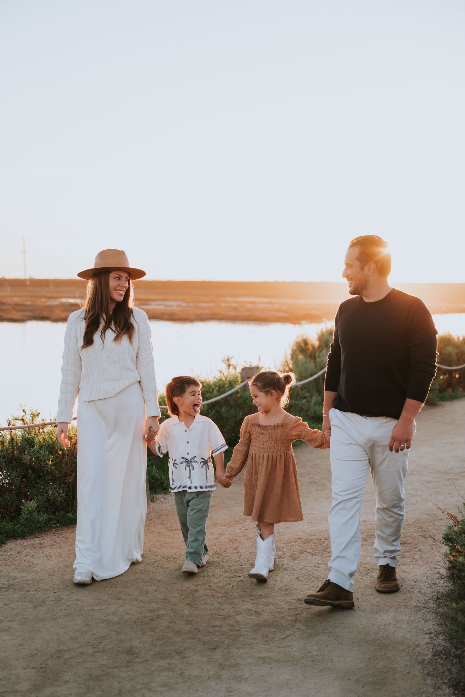 A family walks together on a coastal path during golden hour sunset.