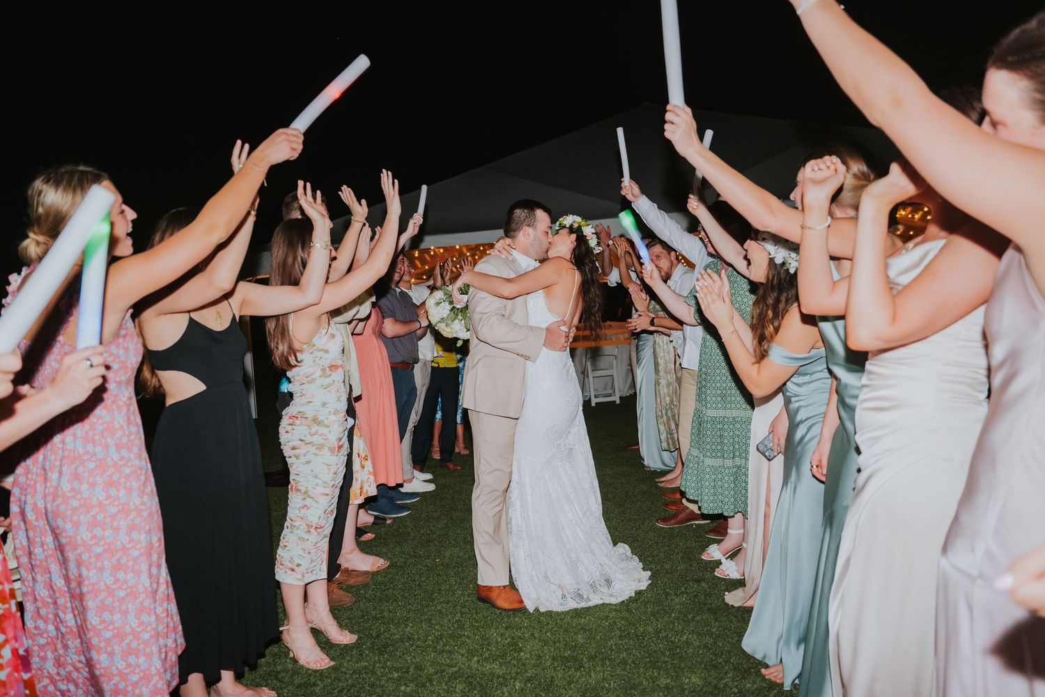 Wedding guests form a glowing tunnel with LED light wands as newlyweds dance through at night.