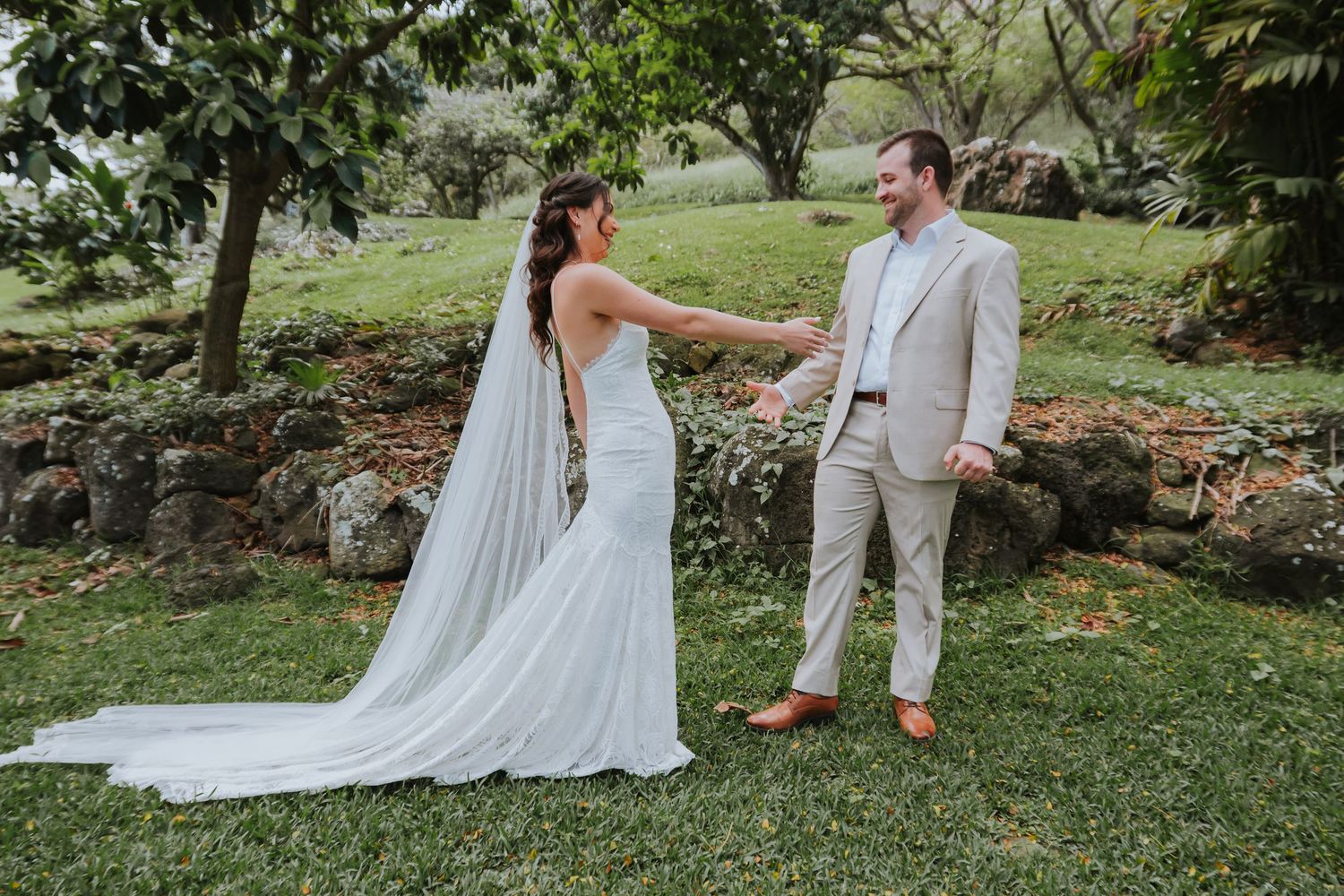 A romantic wedding couple walks together on a lush green lawn surrounded by trees and natural scenery.