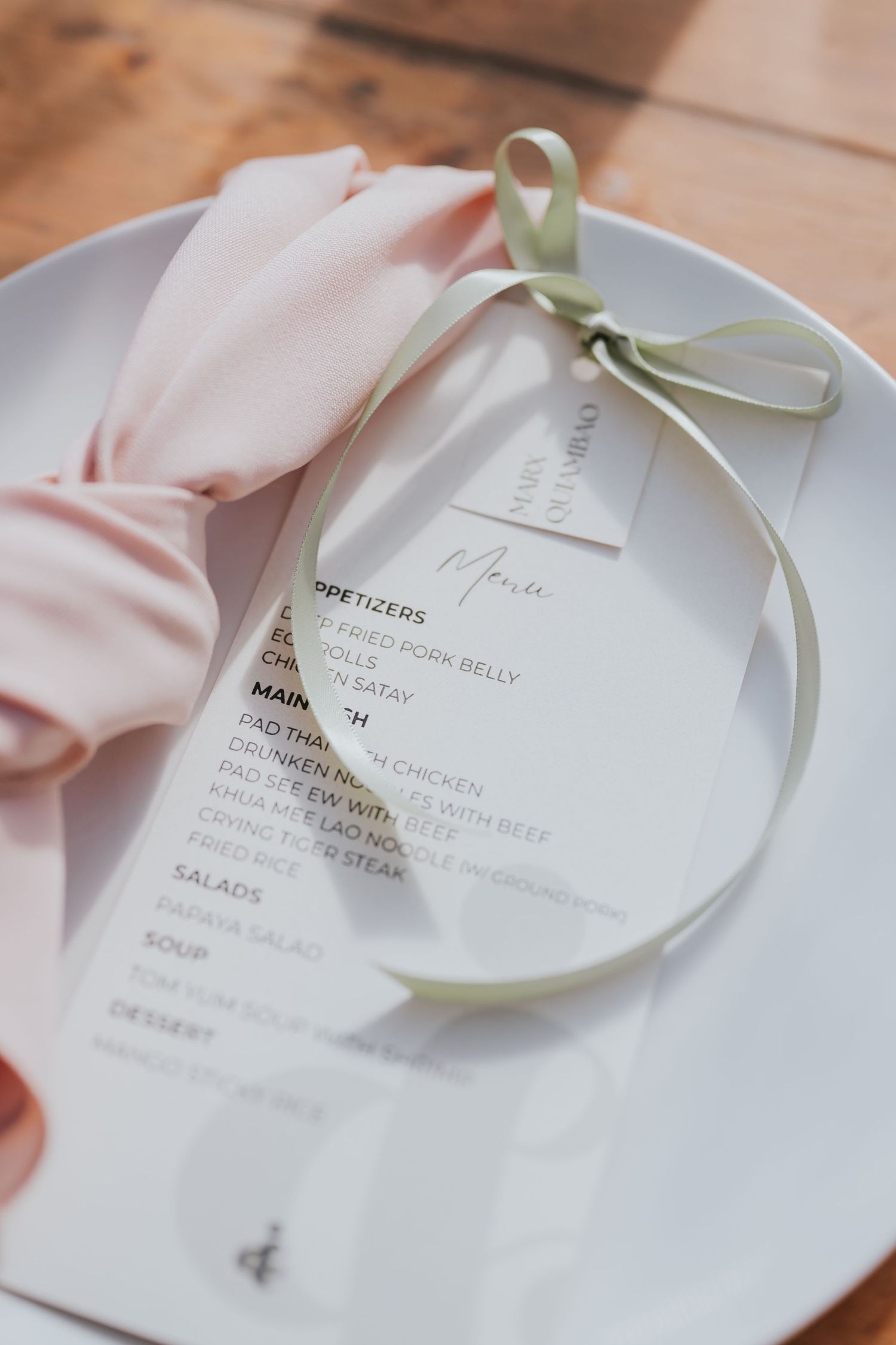 White wedding menu cards with sage green ribbons displayed on elegant place settings at a formal event.